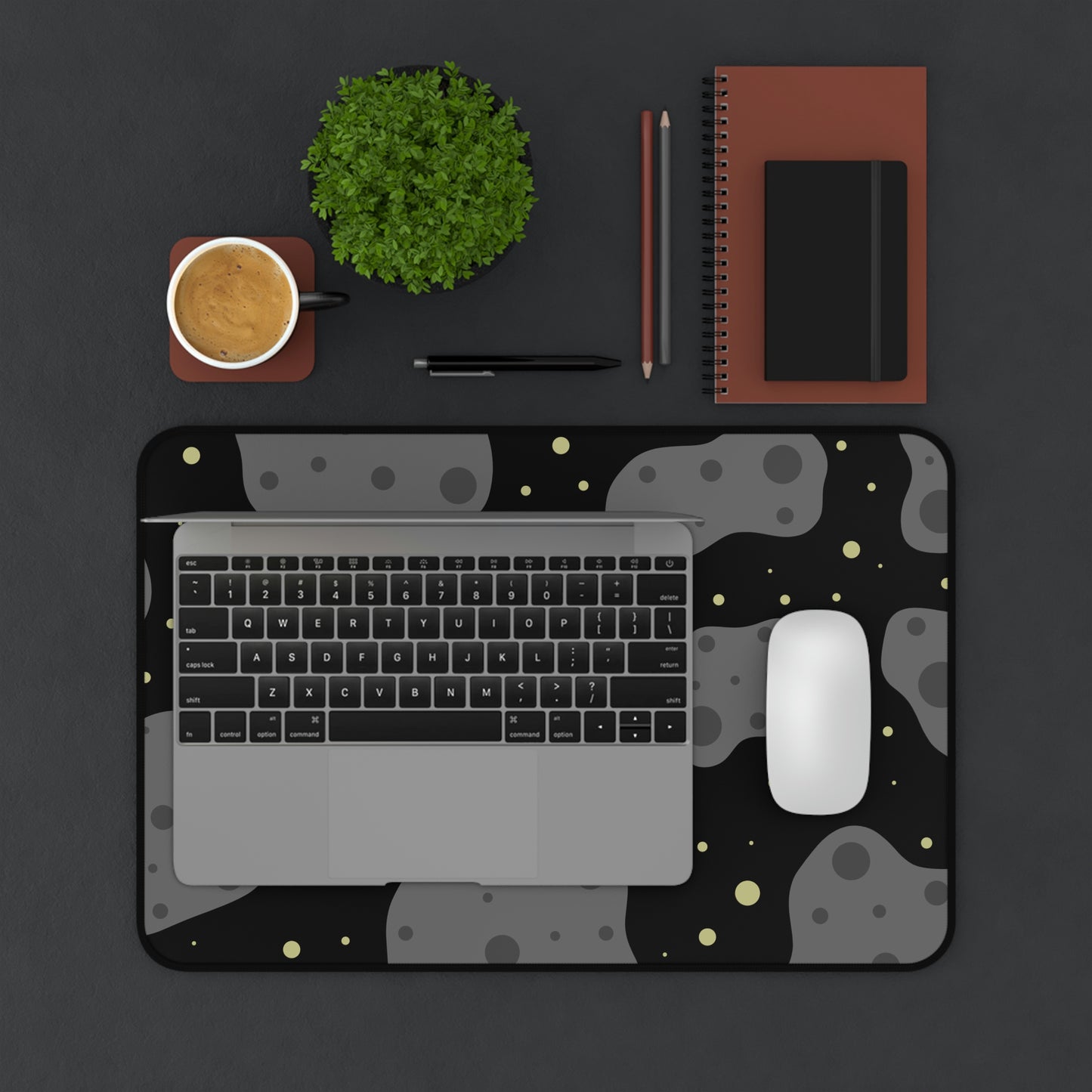 A 12" x 18" desk mat with a black background, gray asteroids, and yellow stars. A laptop and mouse sit on top of it.