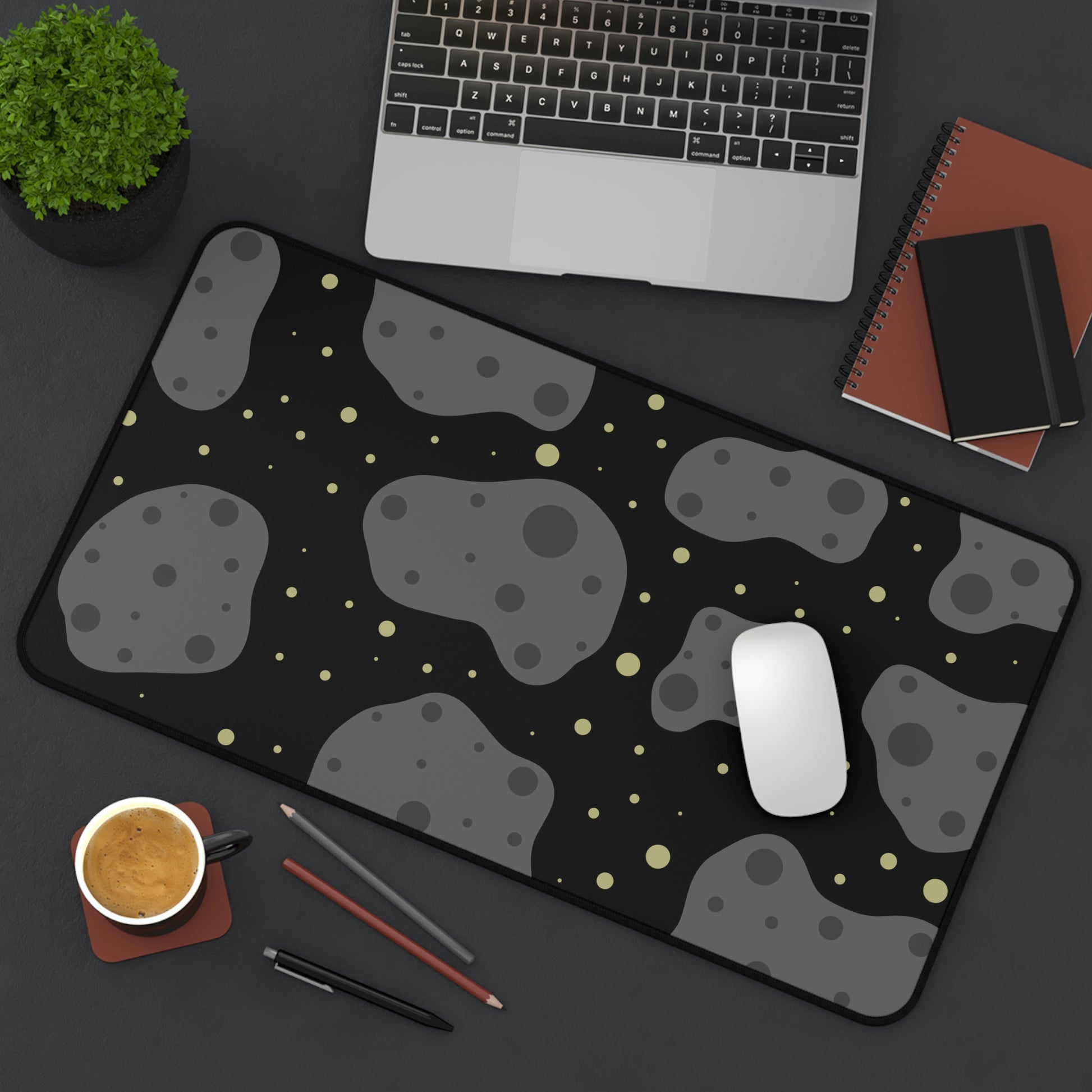 A 12" x 22" desk mat with a black background, gray asteroids, and yellow stars sitting at an angle.