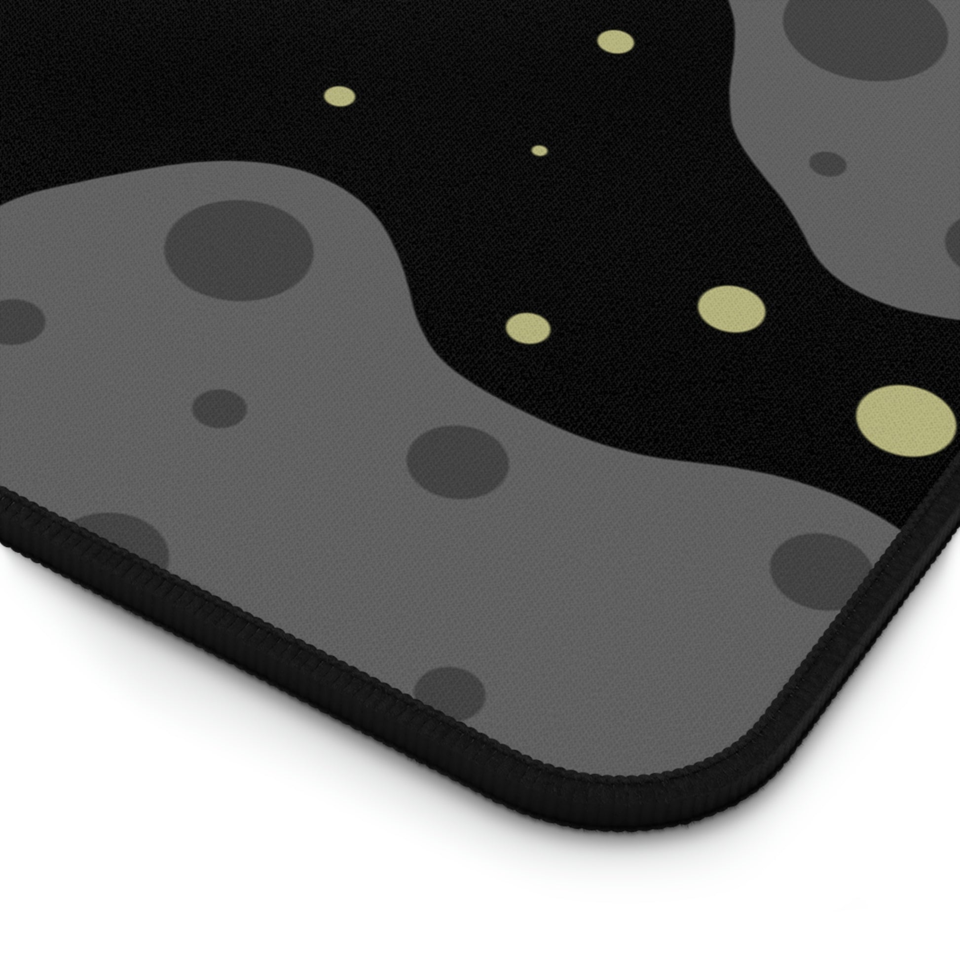 The corner of a 12" x 22" desk mat with a black background, gray asteroids, and yellow stars.