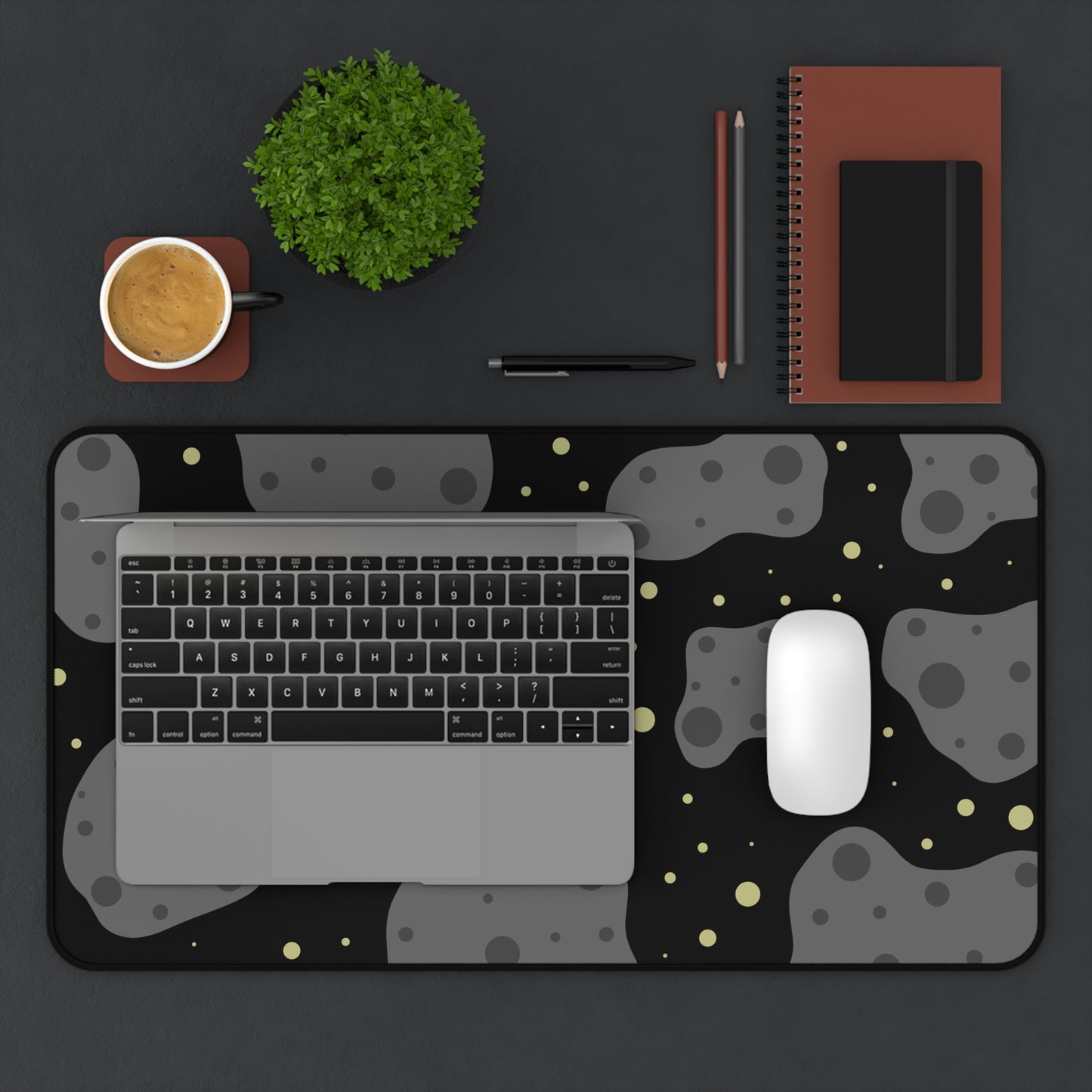 A 12" x 22" desk mat with a black background, gray asteroids, and yellow stars. A laptop and mouse sit on top of it.