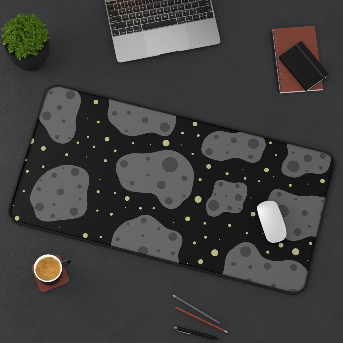 A 31" x 15.5" desk mat with a black background, gray asteroids, and yellow stars sitting at an angle.