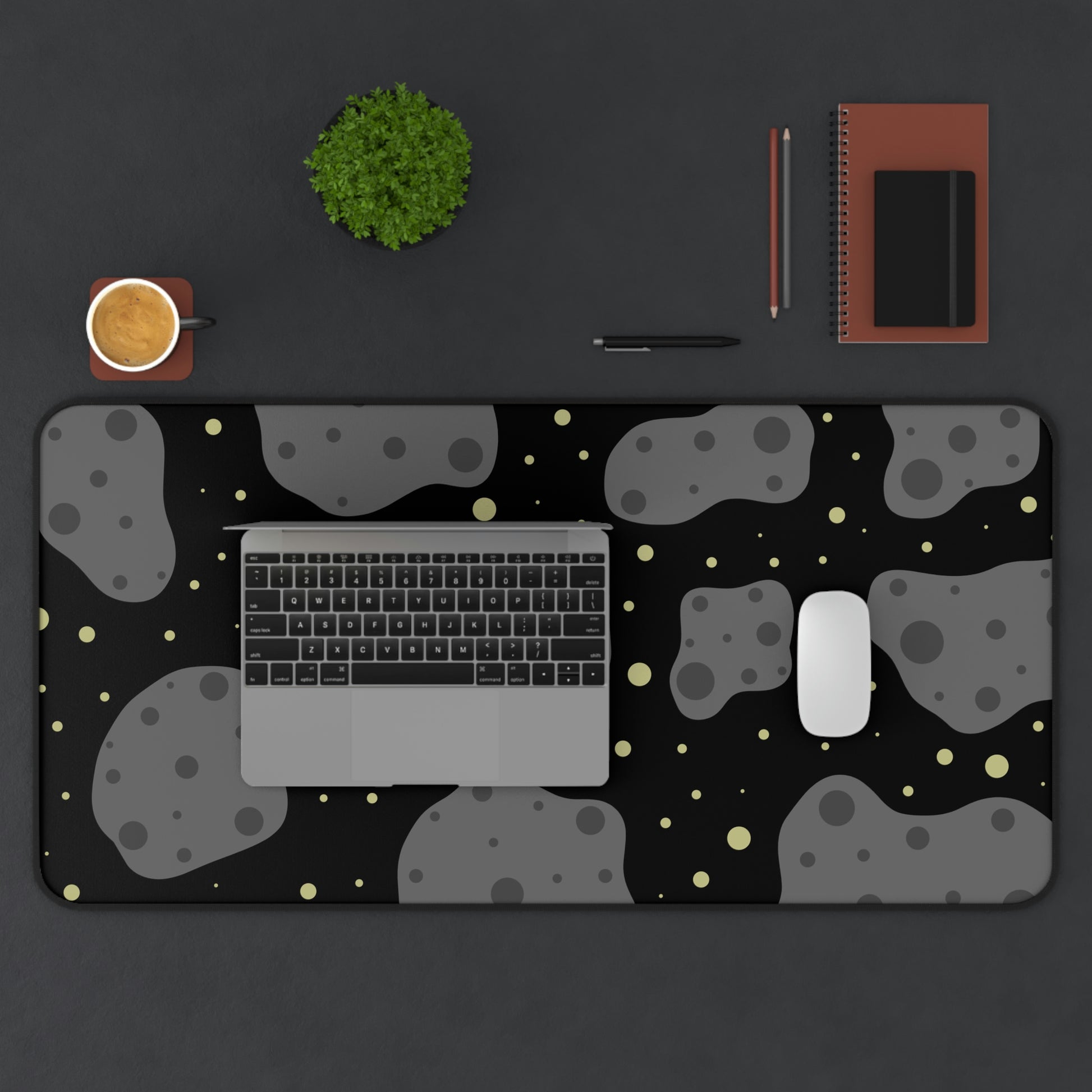 A 31" x 15.5" desk mat with a black background, gray asteroids, and yellow stars. A laptop and mouse sit on top of it.