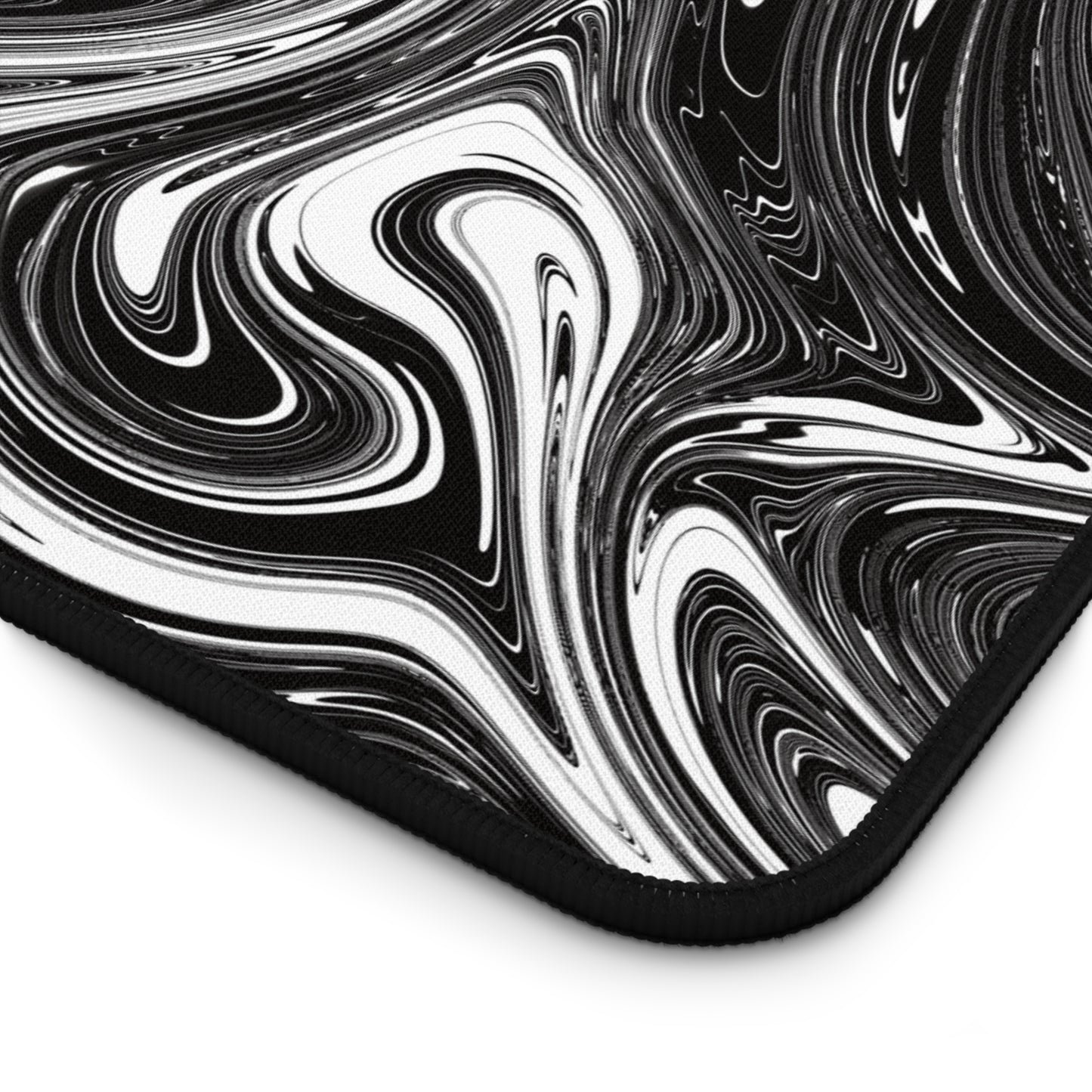 The corner of a 12" x 18" desk mat with black and white swirls.