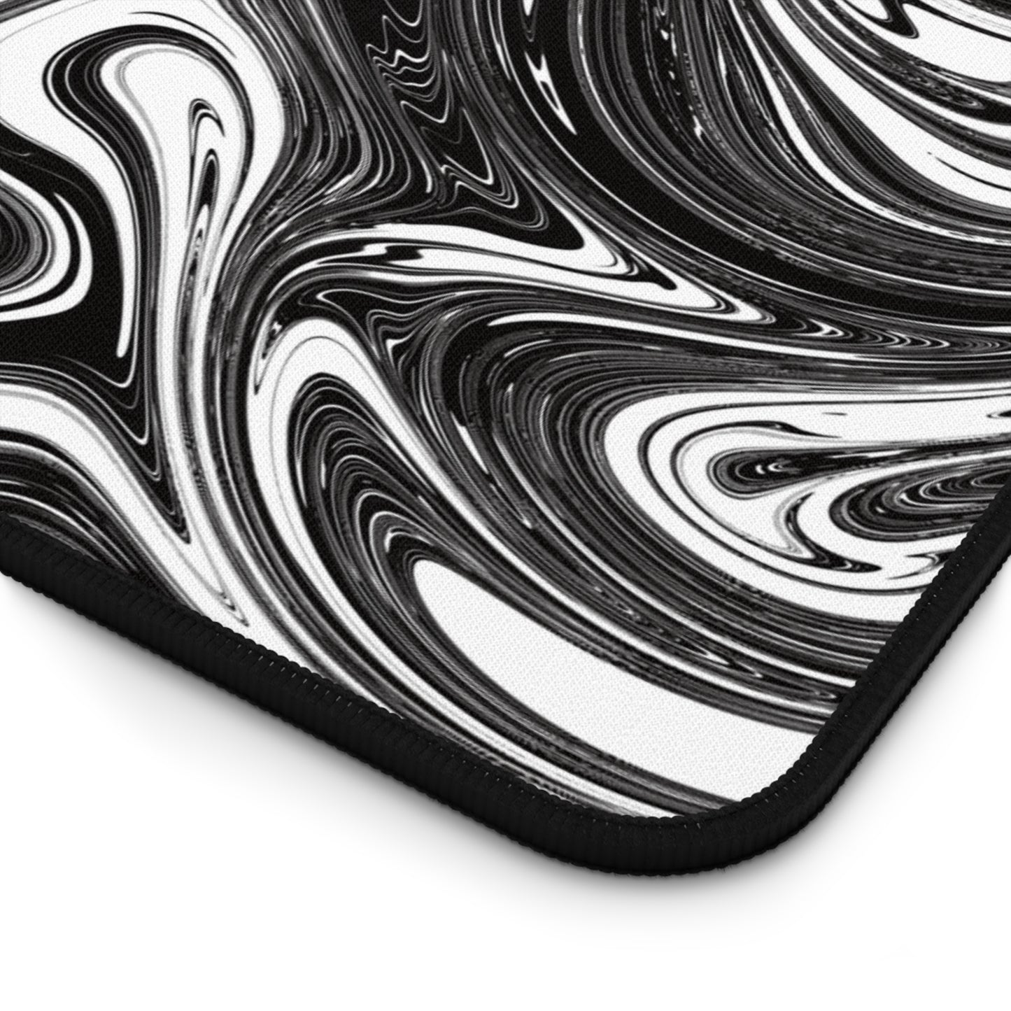 The corner of a 12" x 22" desk mat with black and white swirls.
