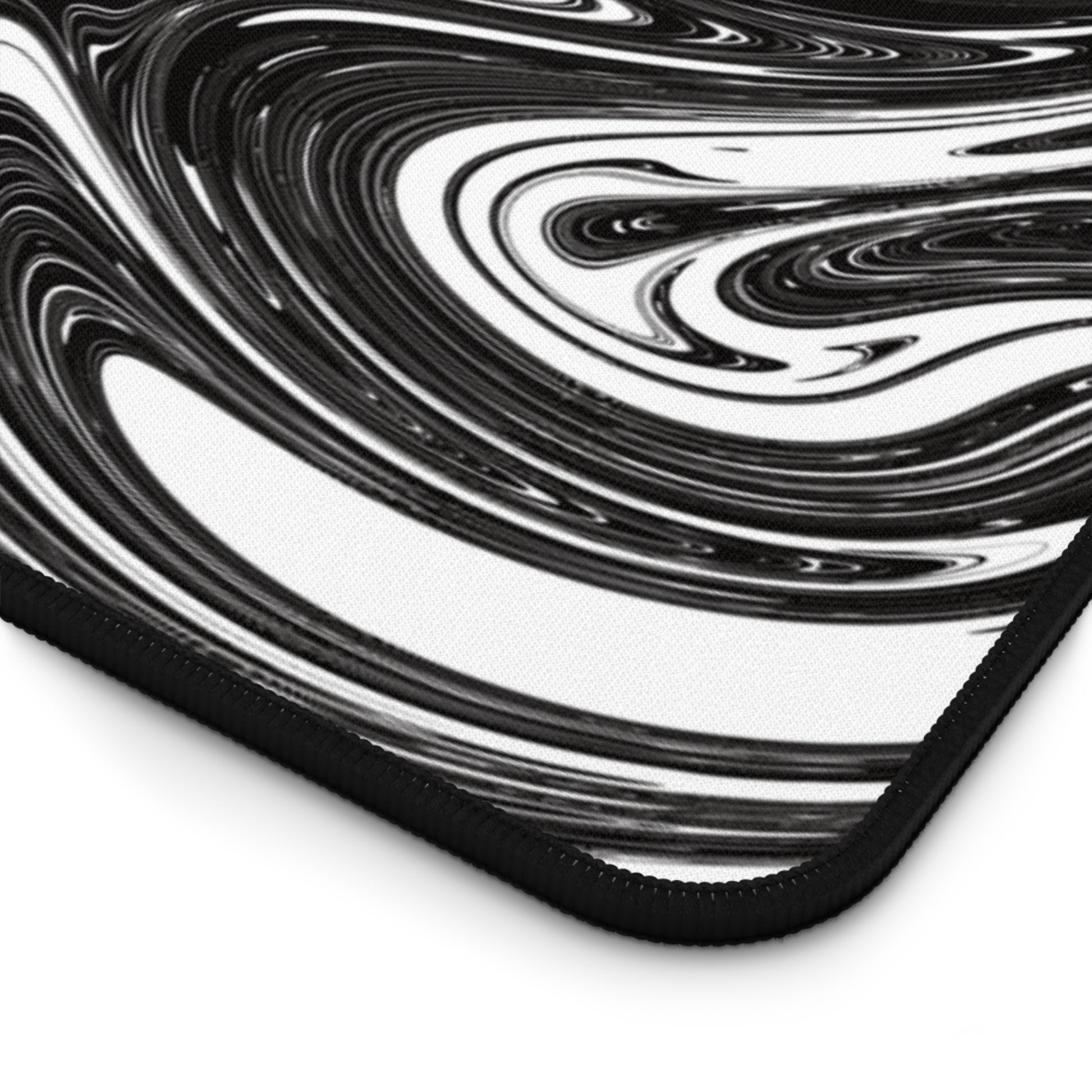 The corner of a 31" x 15.5" desk mat with black and white swirls.