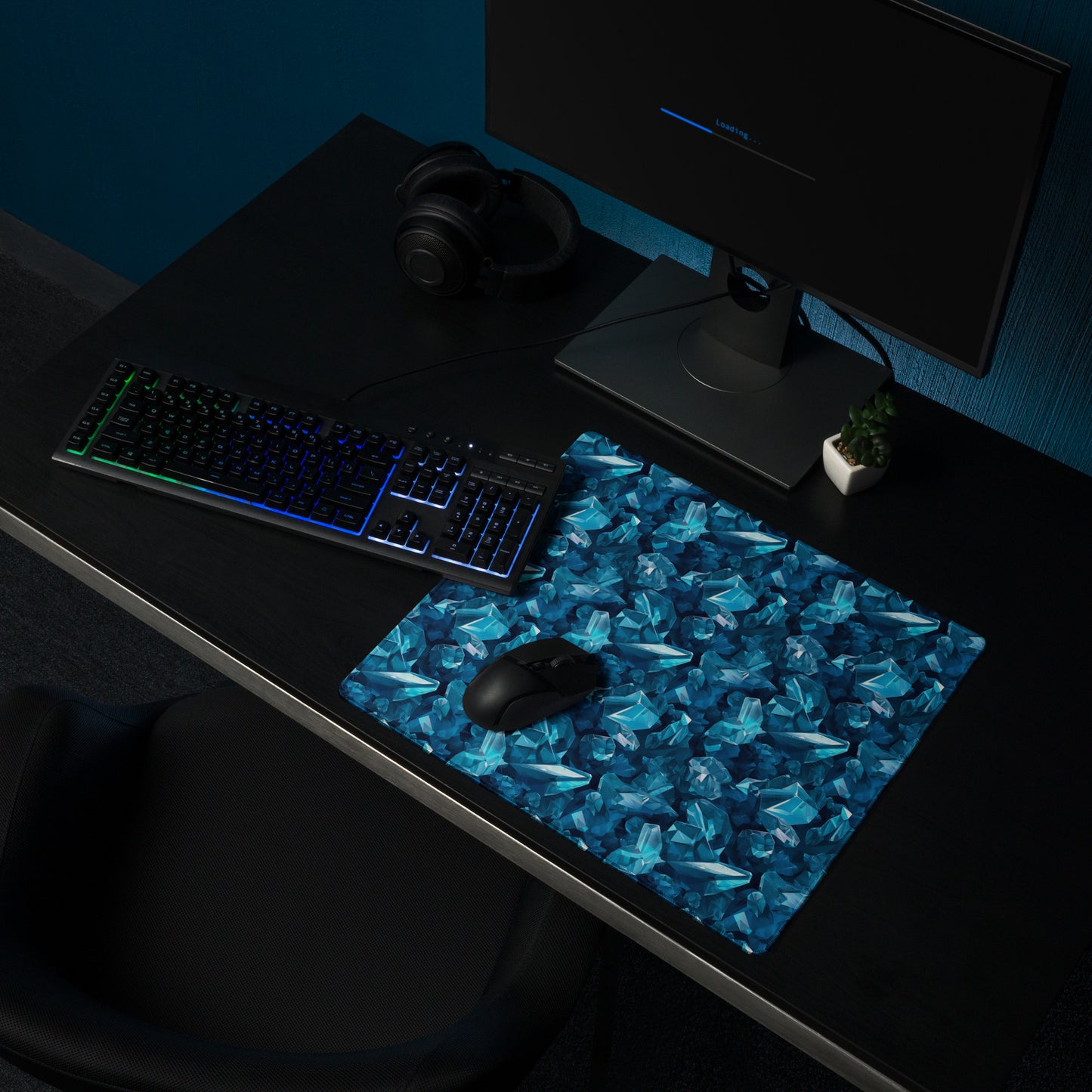 An 18" x 16" gaming desk pad with blue crystals. It sits on a black desk with a monitor, keyboard, and mouse.