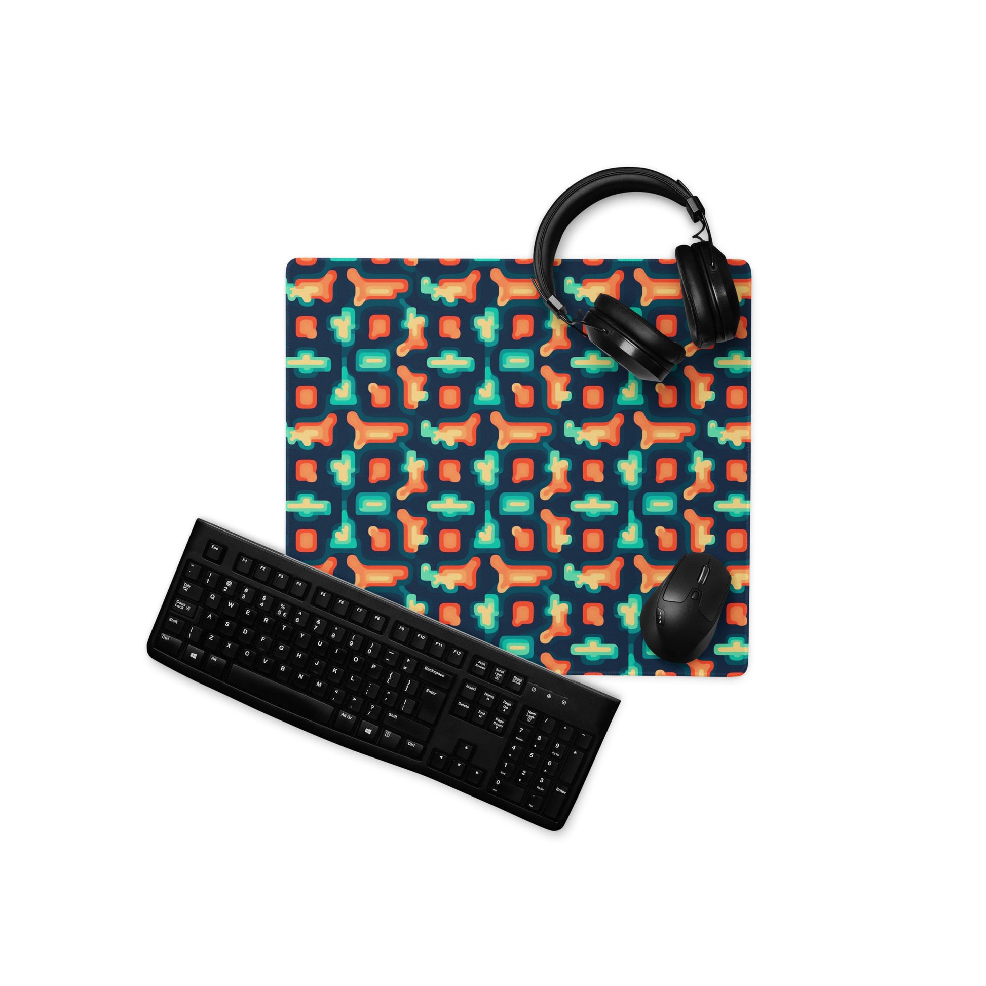 An 18" x 16" gaming desk pad with blue and orange puzzle pieces on a dark blue background. A keyboard, mouse, and headphones sit on it.