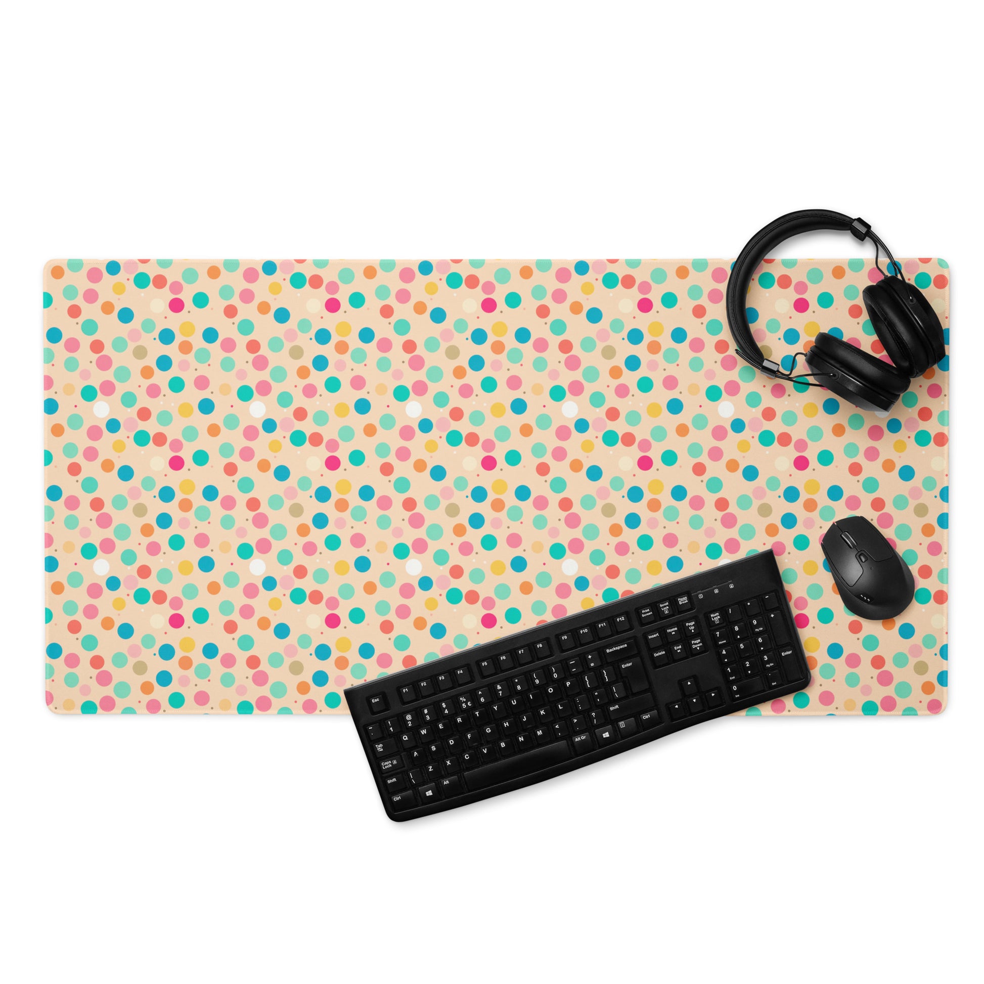 A 36" x 18" desk pad with a colorful polka dot pattern. With a keyboard, mouse, and headphones sitting on it.