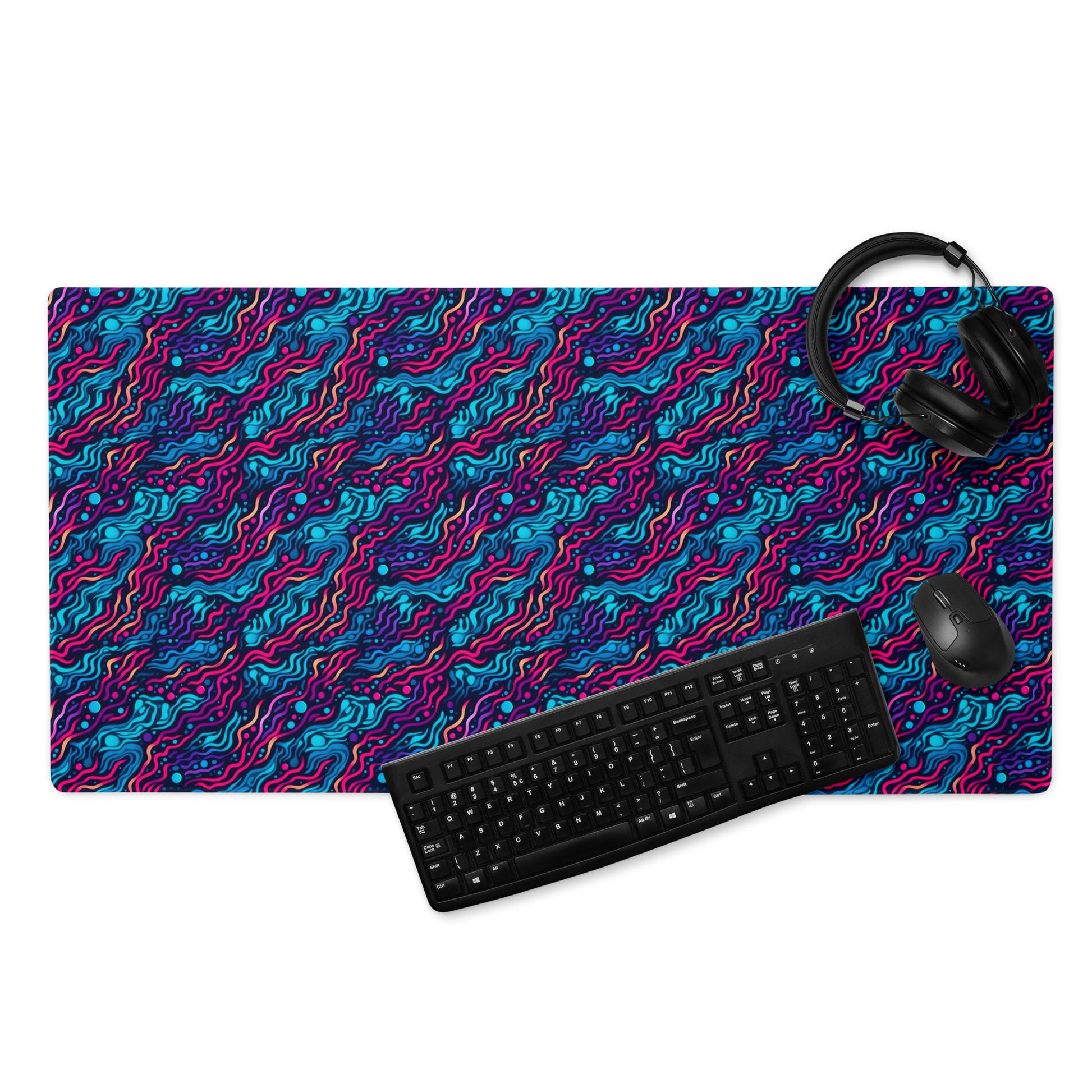 A 36" x 18" desk pad with wavy blue and pink pattern. With a keyboard, mouse, and headphones sitting on it.
