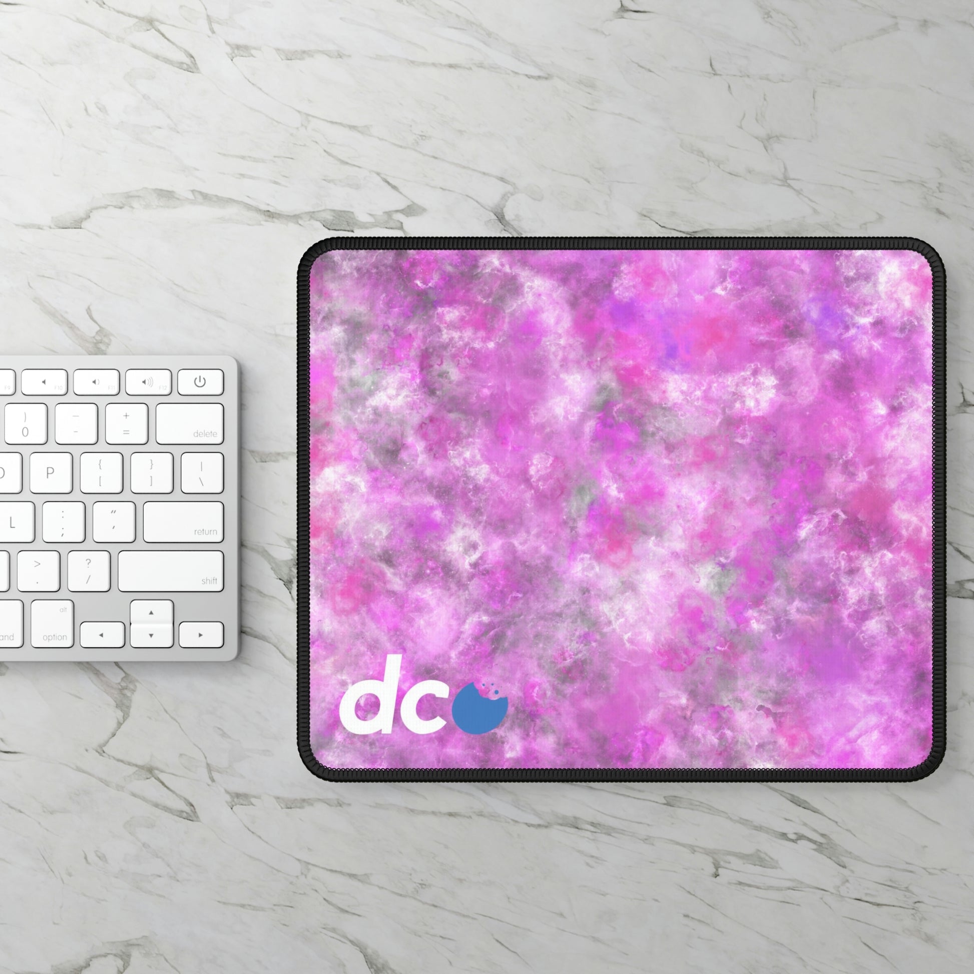 A gaming mouse pad with a fluffy mix of pink, white, and gray sitting next to a keyboard.