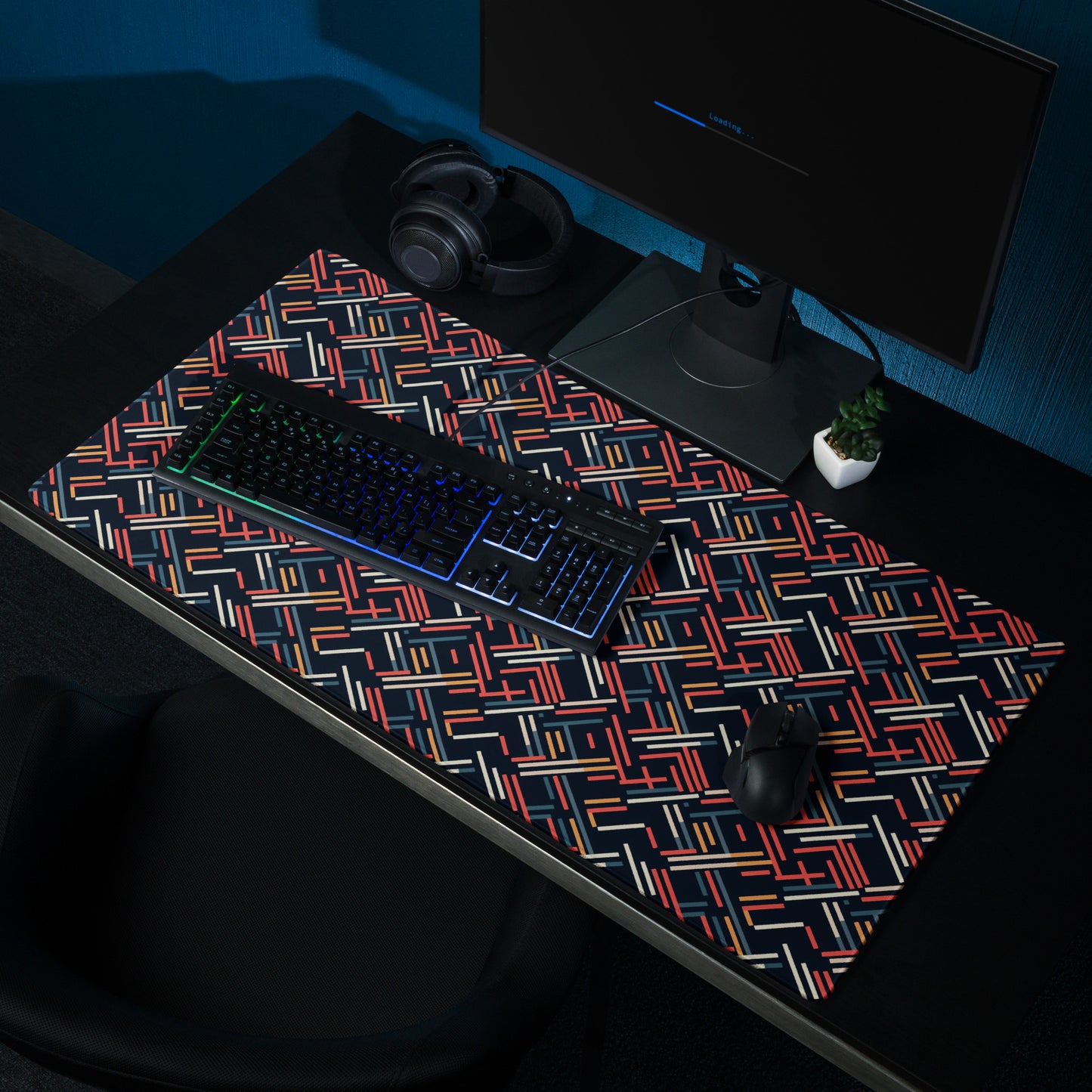 A 36" x 18" gaming desk pad with red, blue, white, and orange lines on a black background. It sits on a black desk with a monitor, keyboard, and mouse.