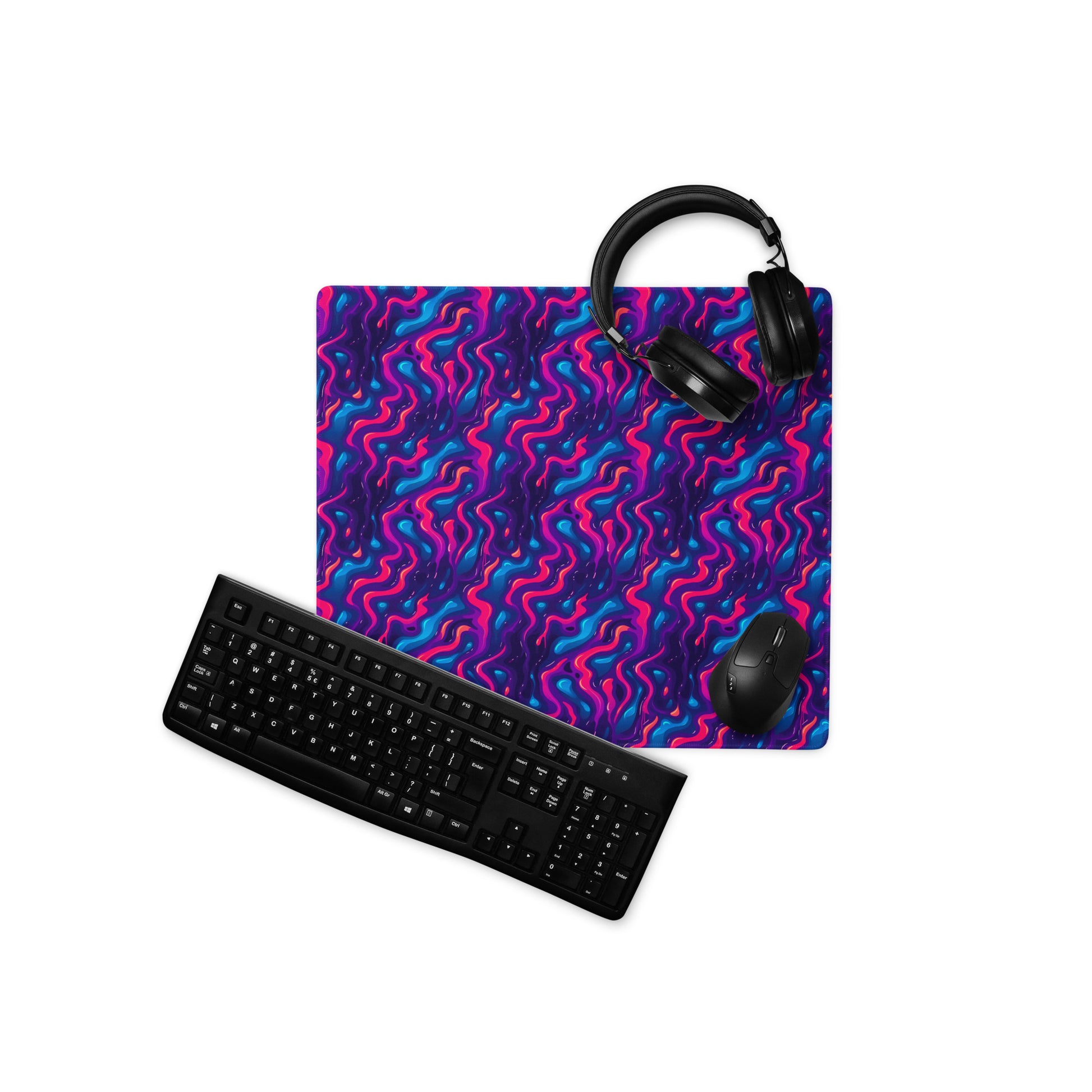A 18" x 16" desk pad with a pink, blue and purple wavy pattern. With a keyboard, mouse, and headphones sitting on it.