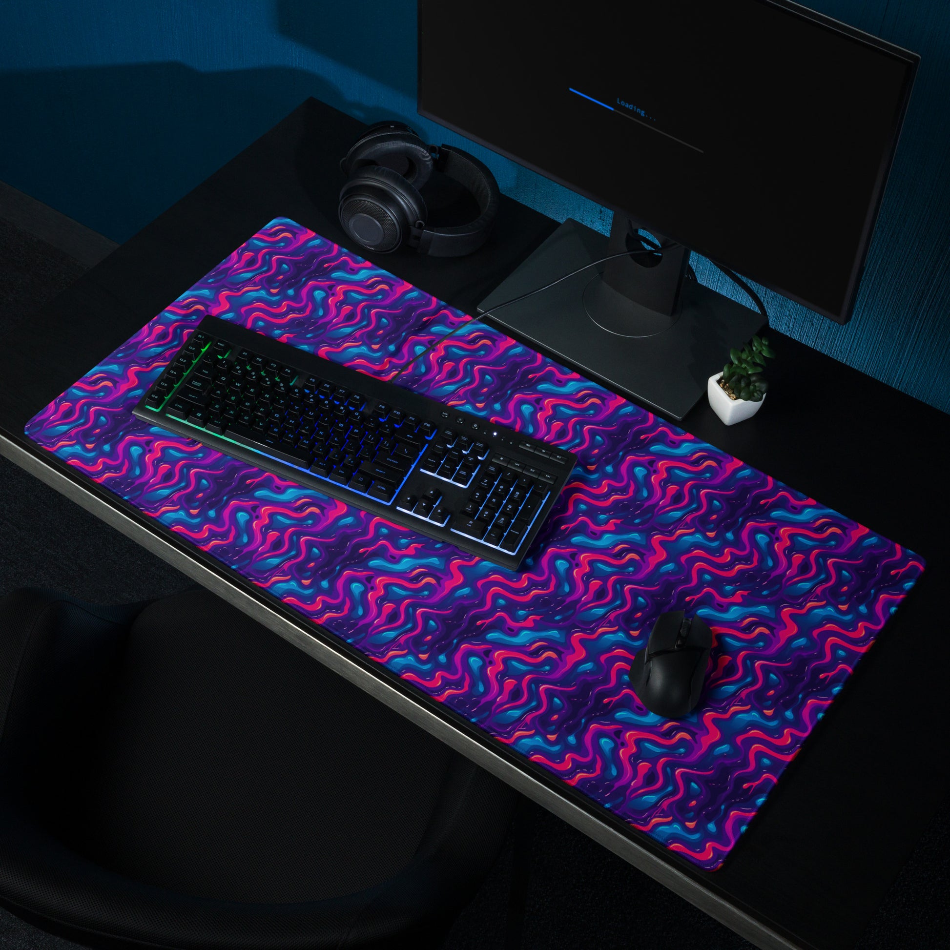 A 36" x 18" desk pad with a pink, blue and purple wavy pattern sitting on a desk.