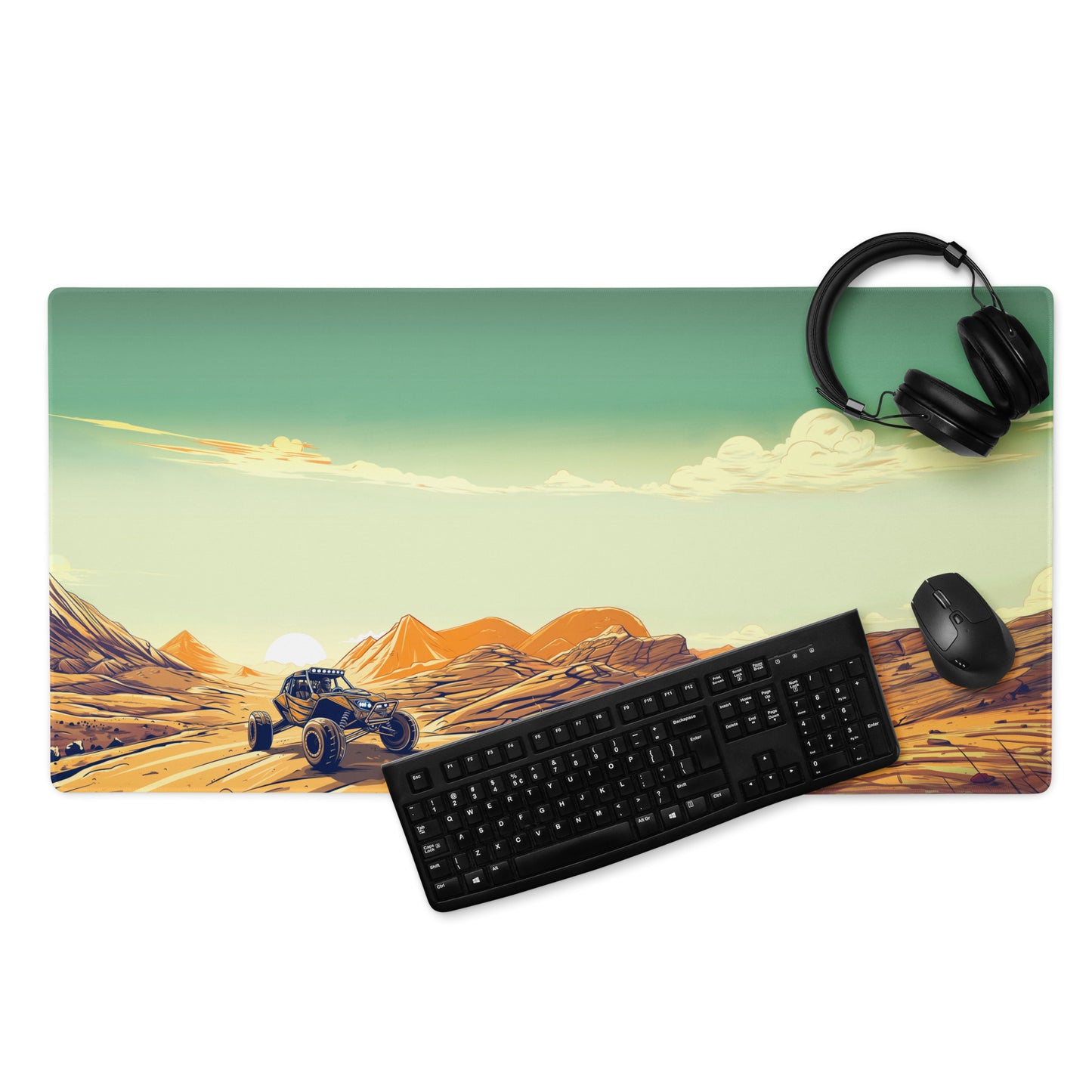 A 36" x 18" desk pad with a dune buggy in a desert landscape. With a keyboard, mouse, and headphones sitting on it.