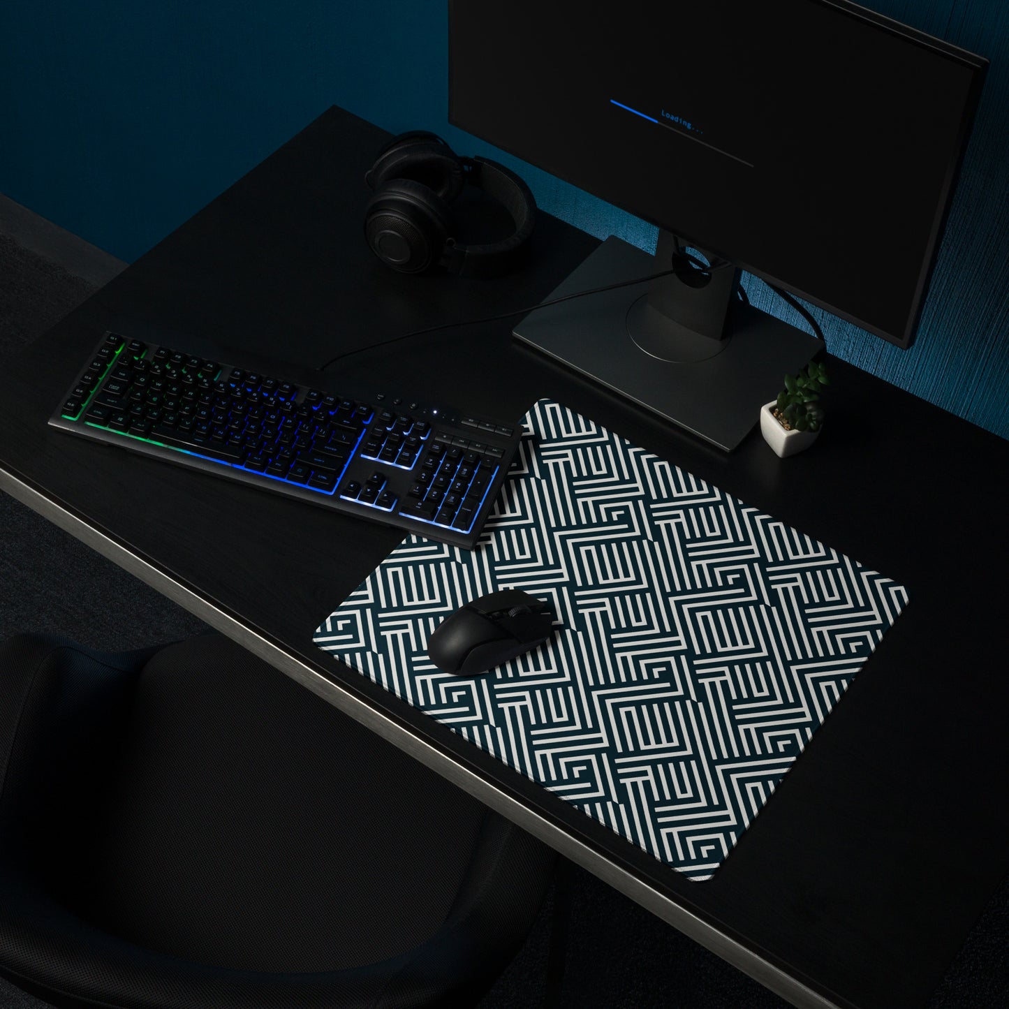 An 18" x 16" gaming desk pad with white lines on a black background. It sits on a black desk with a keyboard, monitor, and mouse.