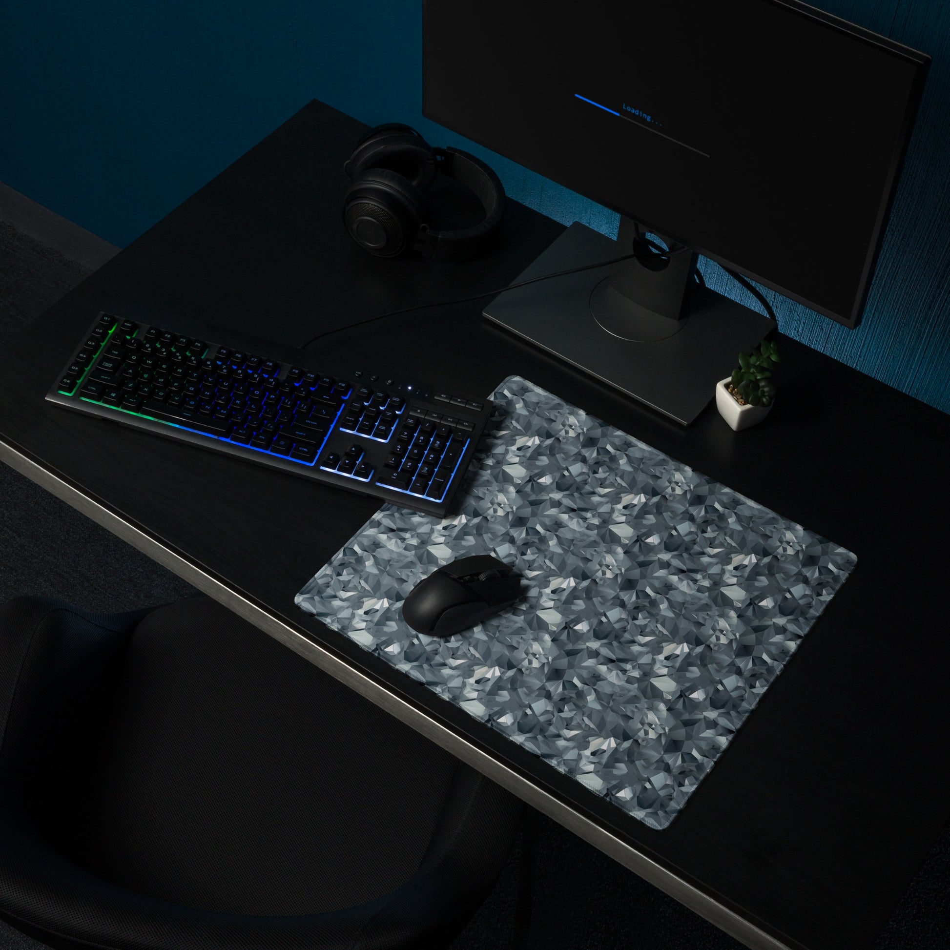 An 18" x 16" gaming desk pad with gray crystals. It sits on a black desk with a monitor, keyboard, and mouse.