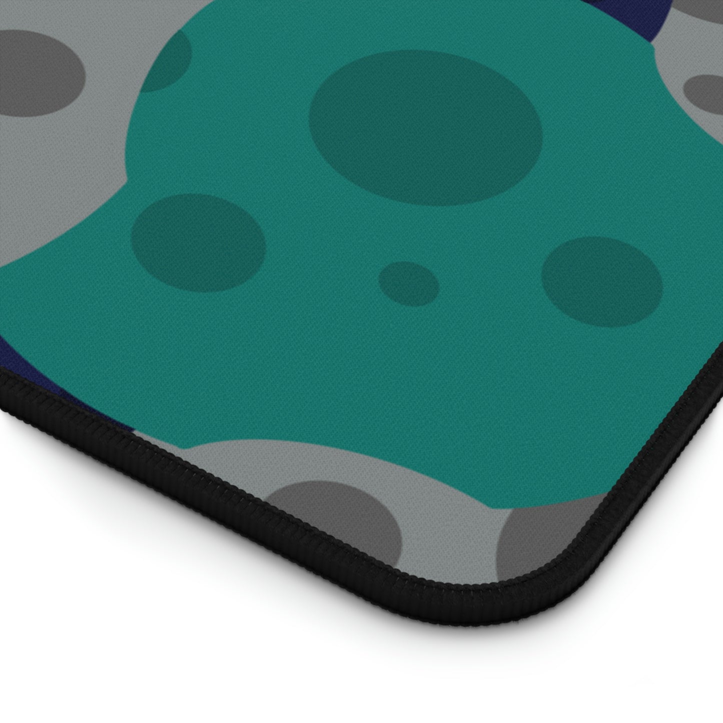 The corner of a 12" x 22" desk mat with gray, teal, and dark blue meteorites.