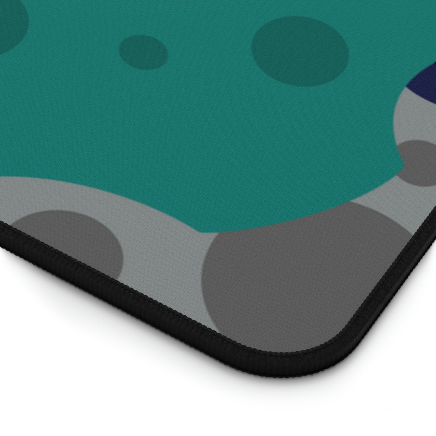 The corner of a 31" x 15.5" desk mat with gray, teal, and dark blue meteorites.