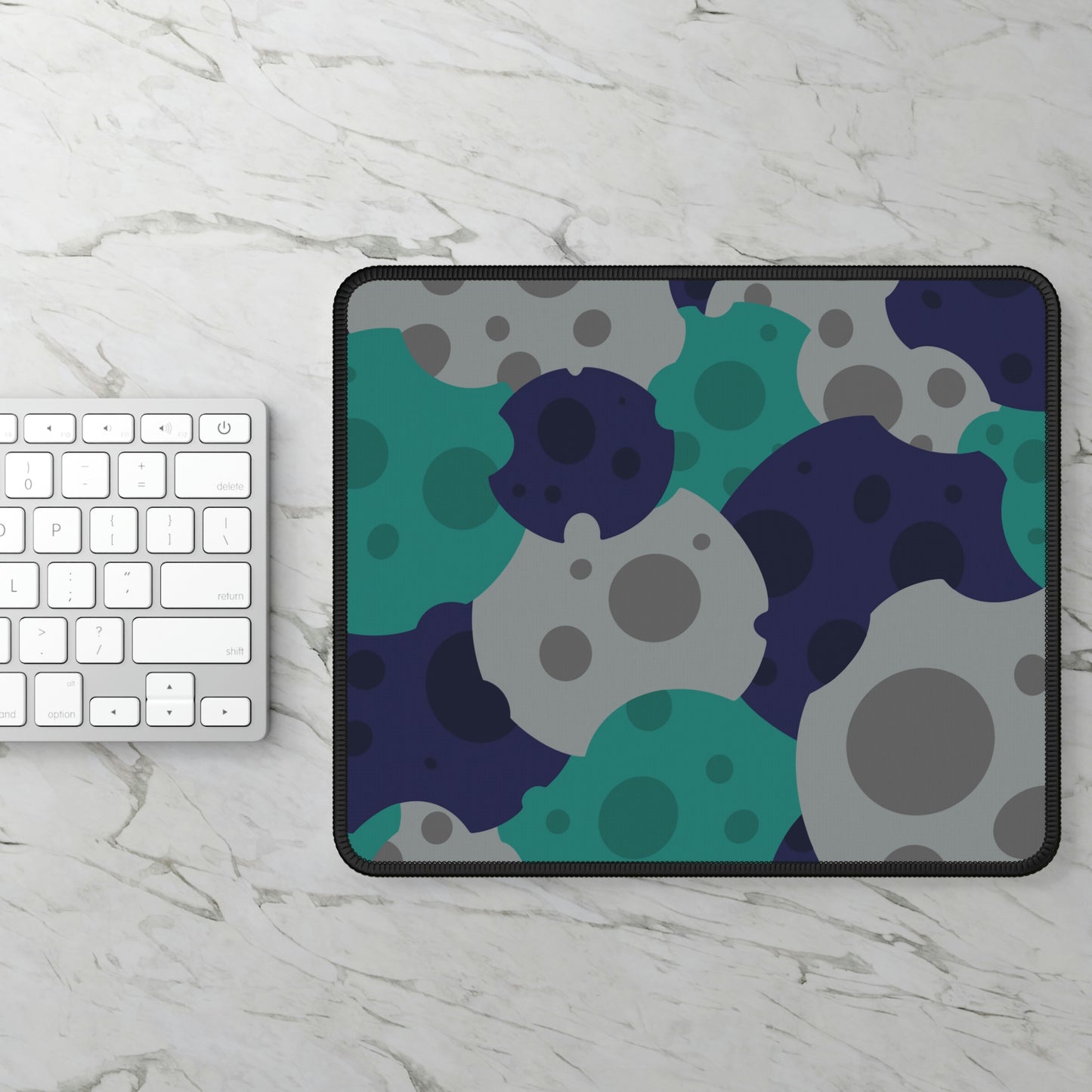 A gaming mouse pad with gray, teal, and dark blue meteorites sitting next to a keyboard.