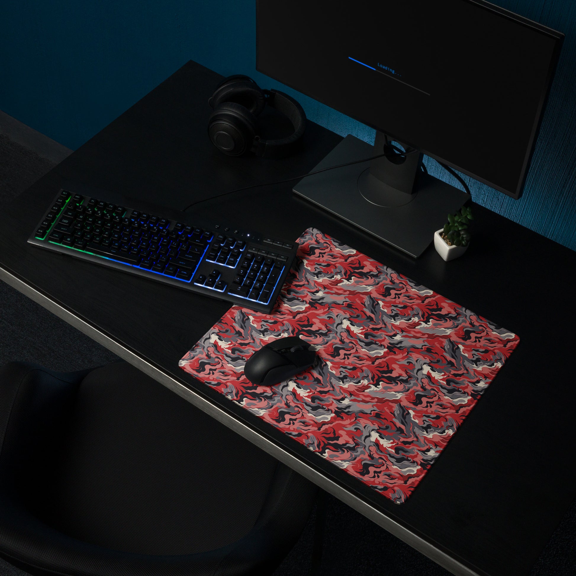 A 18" x 16" desk pad with a grey and red camo pattern sitting on a desk.