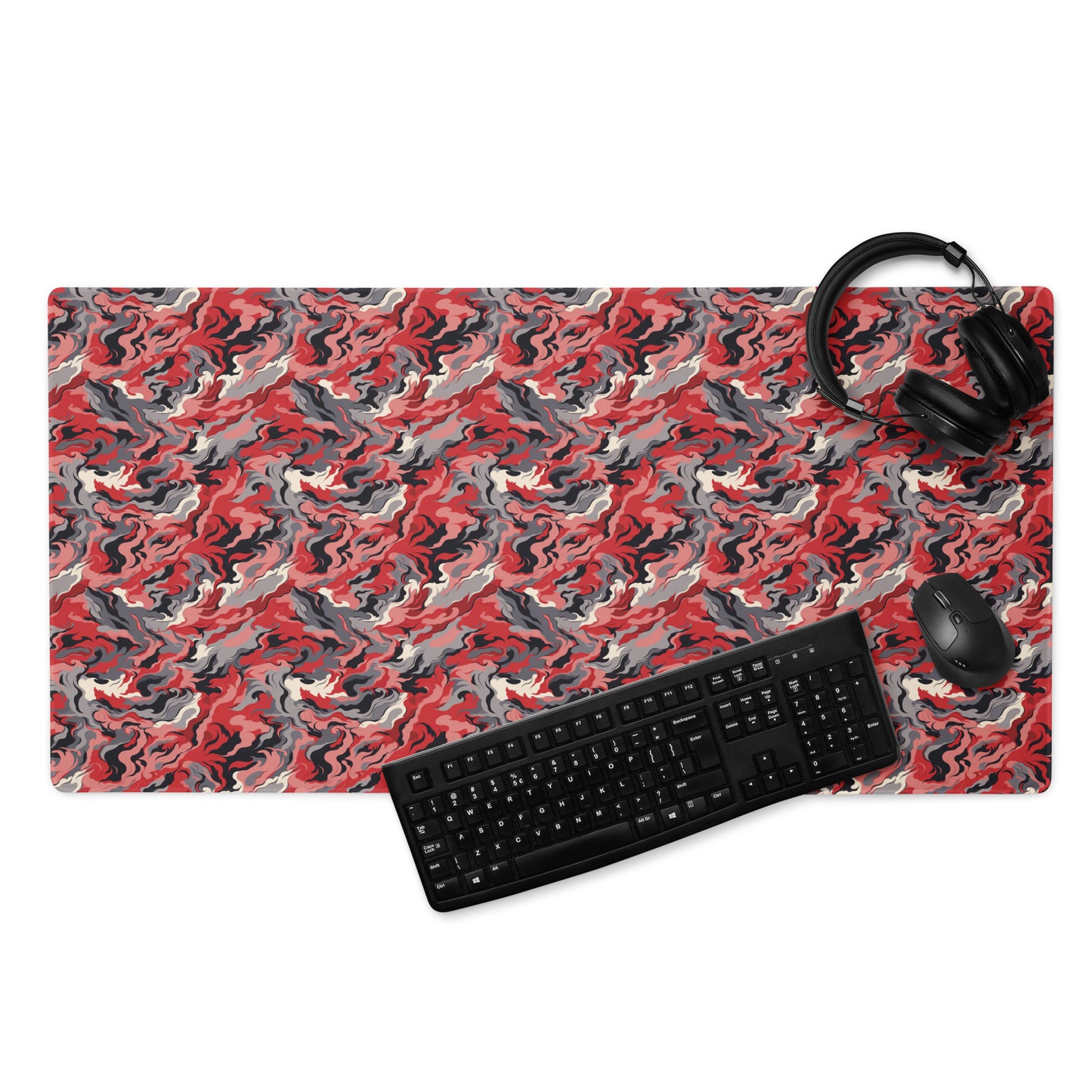 A 36" x 18" desk pad with a grey and red camo pattern. With a keyboard, mouse, and headphones sitting on it.