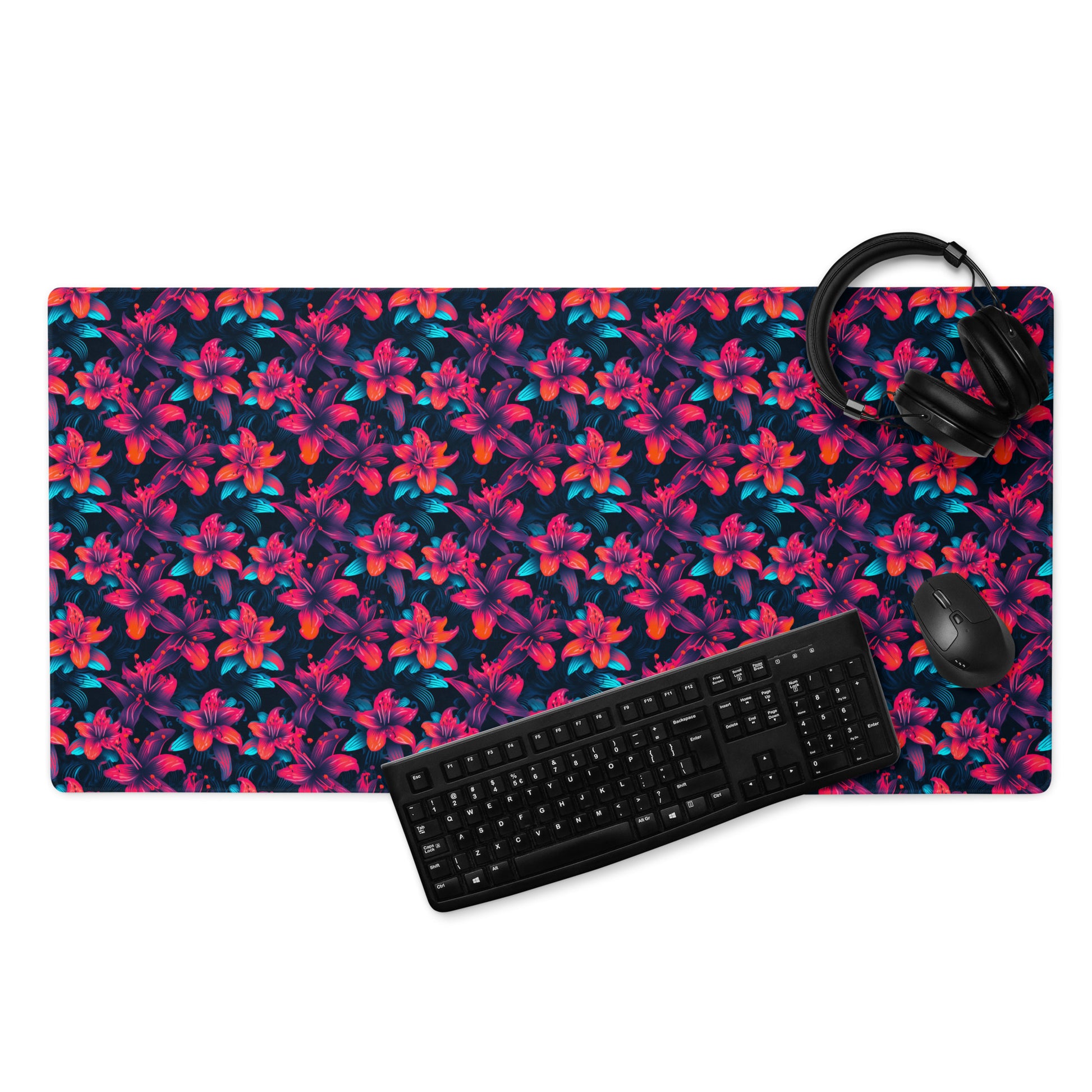 A 36" x 18" desk pad with a neon red and blue floral pattern. With a keyboard, mouse, and headphones sitting on it.