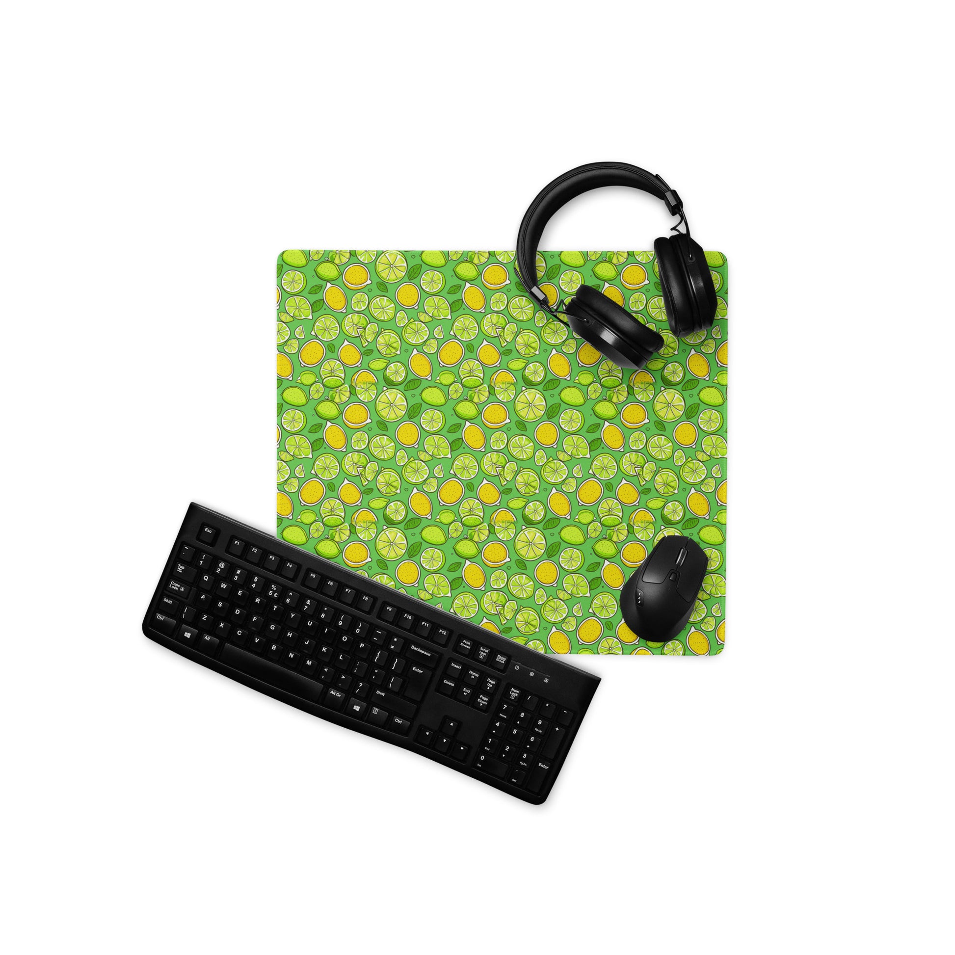 An 18" x 16" gaming desk pad with lemons and limes on a green background. A keyboard, mouse, and headphones sit on it.