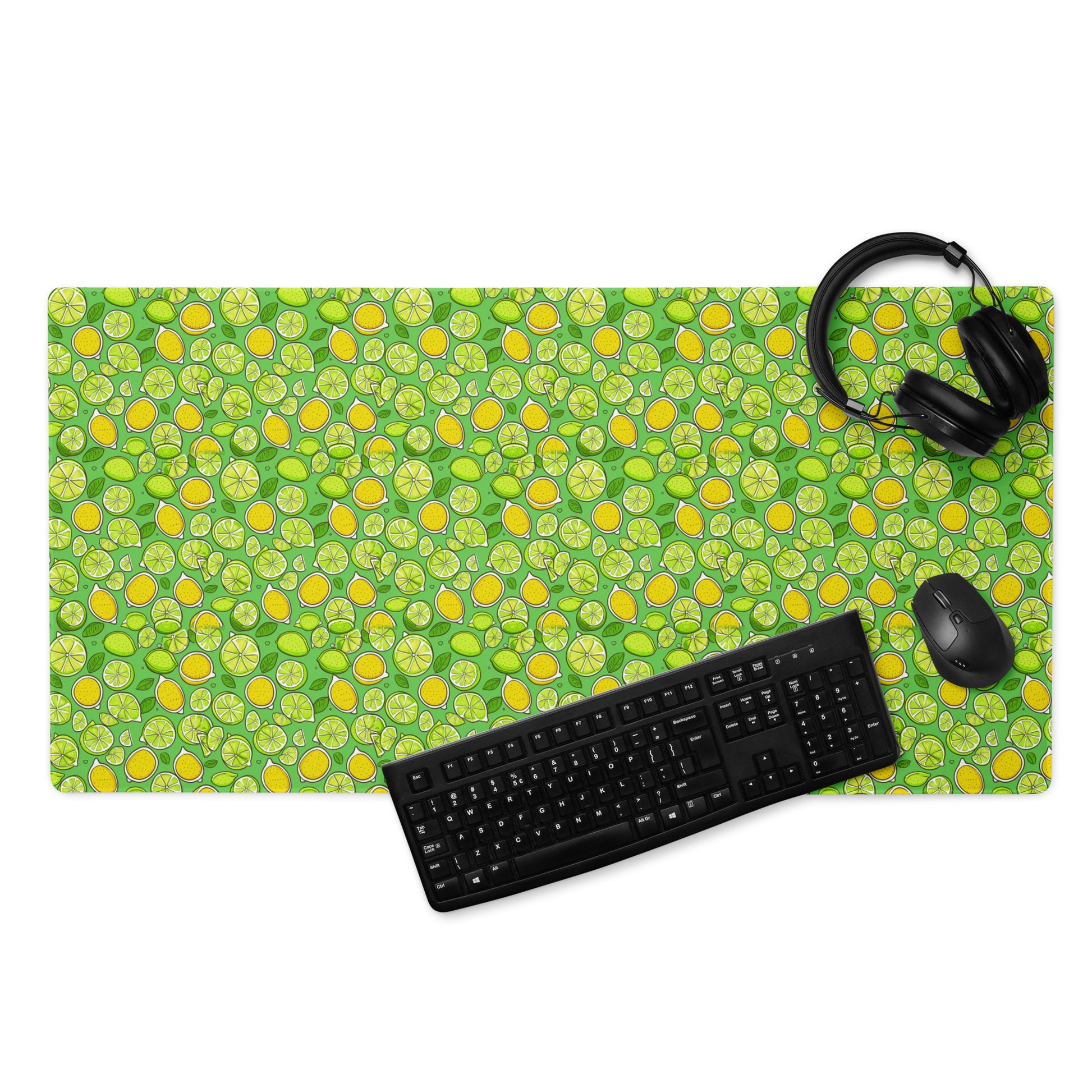 A 36" x 18" gaming desk pad with lemons and limes on a green background. A keyboard, mouse, and headphones sit on it.