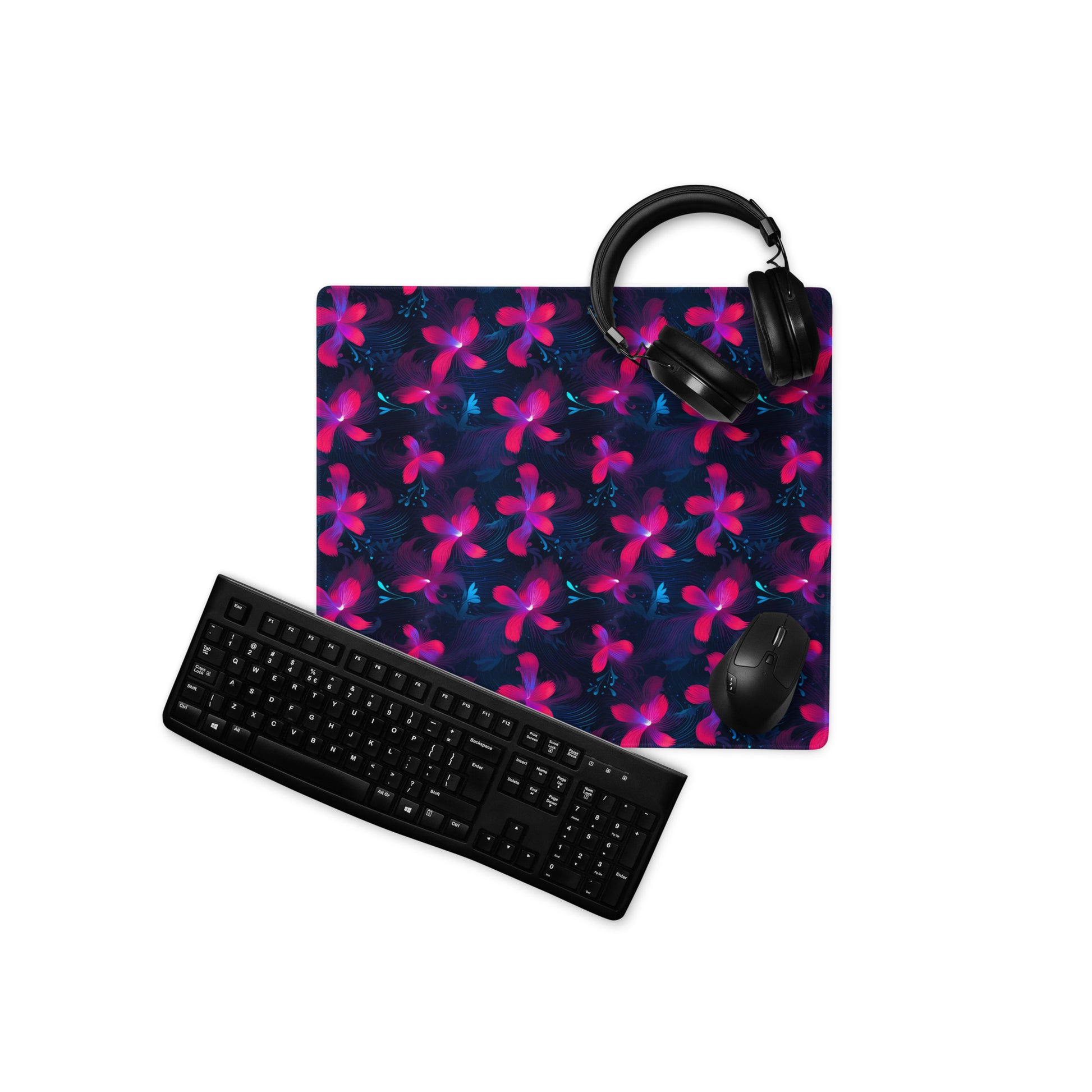 A 18" x 16" desk pad with neon pink and blue floral pattern. With a keyboard, mouse, and headphones sitting on it.