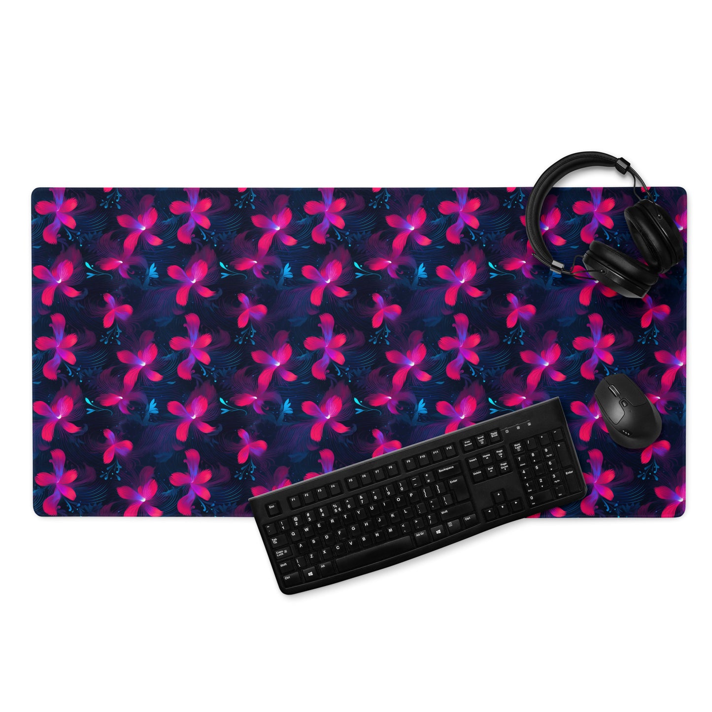 A 36" x 18" desk pad with neon pink and blue floral pattern. With a keyboard, mouse, and headphones sitting on it.