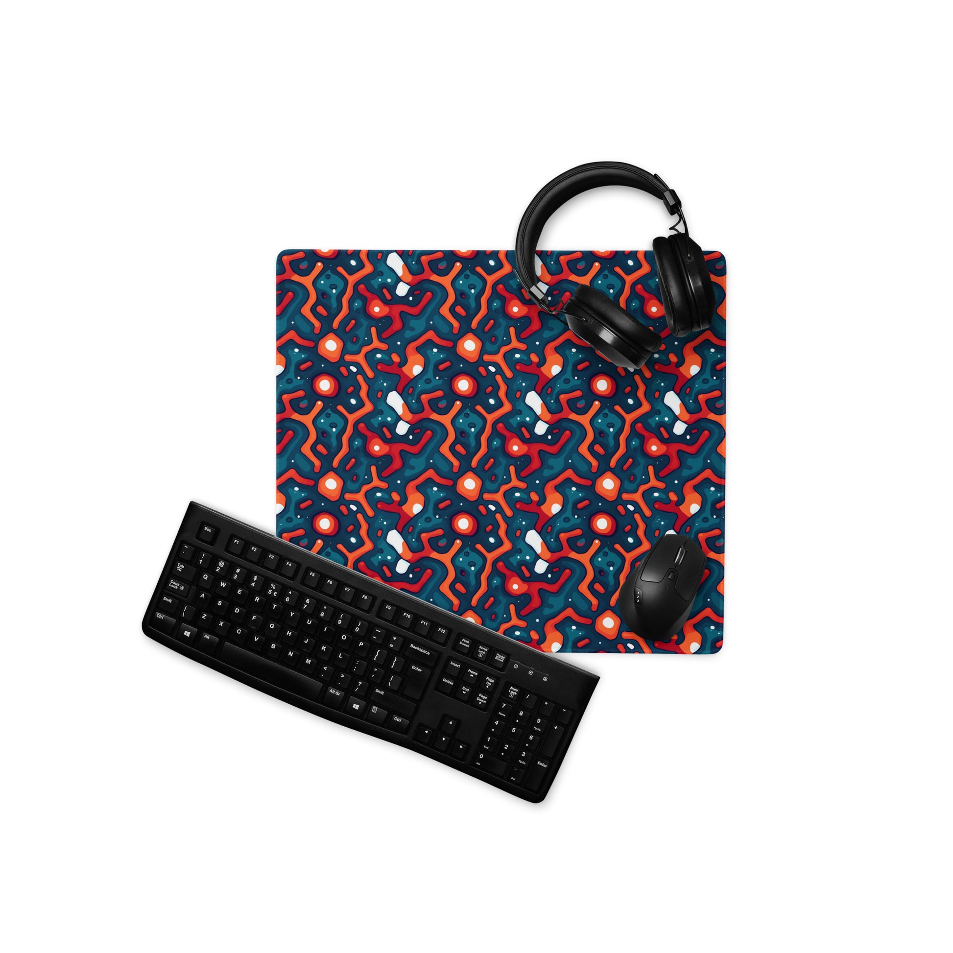 A 18" x 16" desk pad with a blue and orange crack pattern. With a keyboard, mouse, and headphones sitting on it.