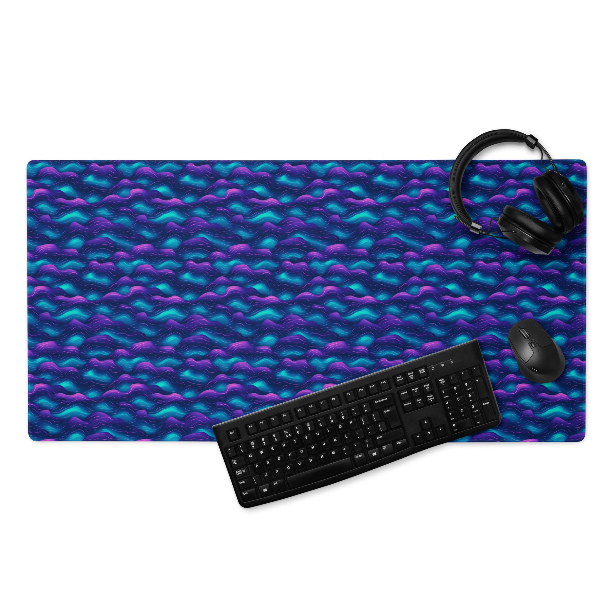 A 36" x 18" desk pad with blue and purple wave pattern. With a keyboard, mouse, and headphones sitting on it.