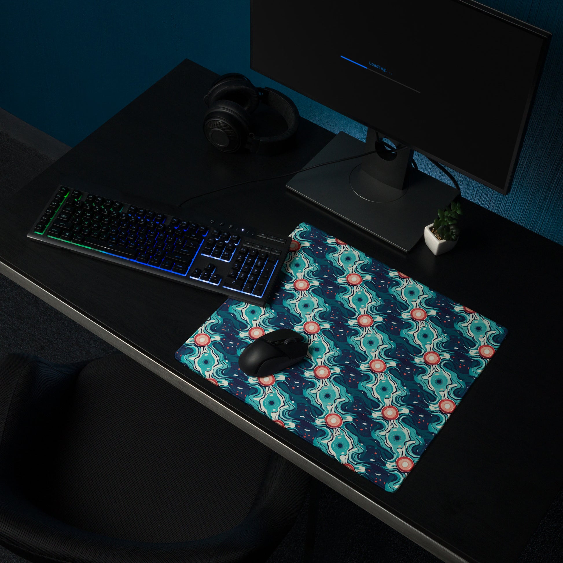 A 18" x 16" desk pad with a teal abstract wavy pattern sitting on a desk.