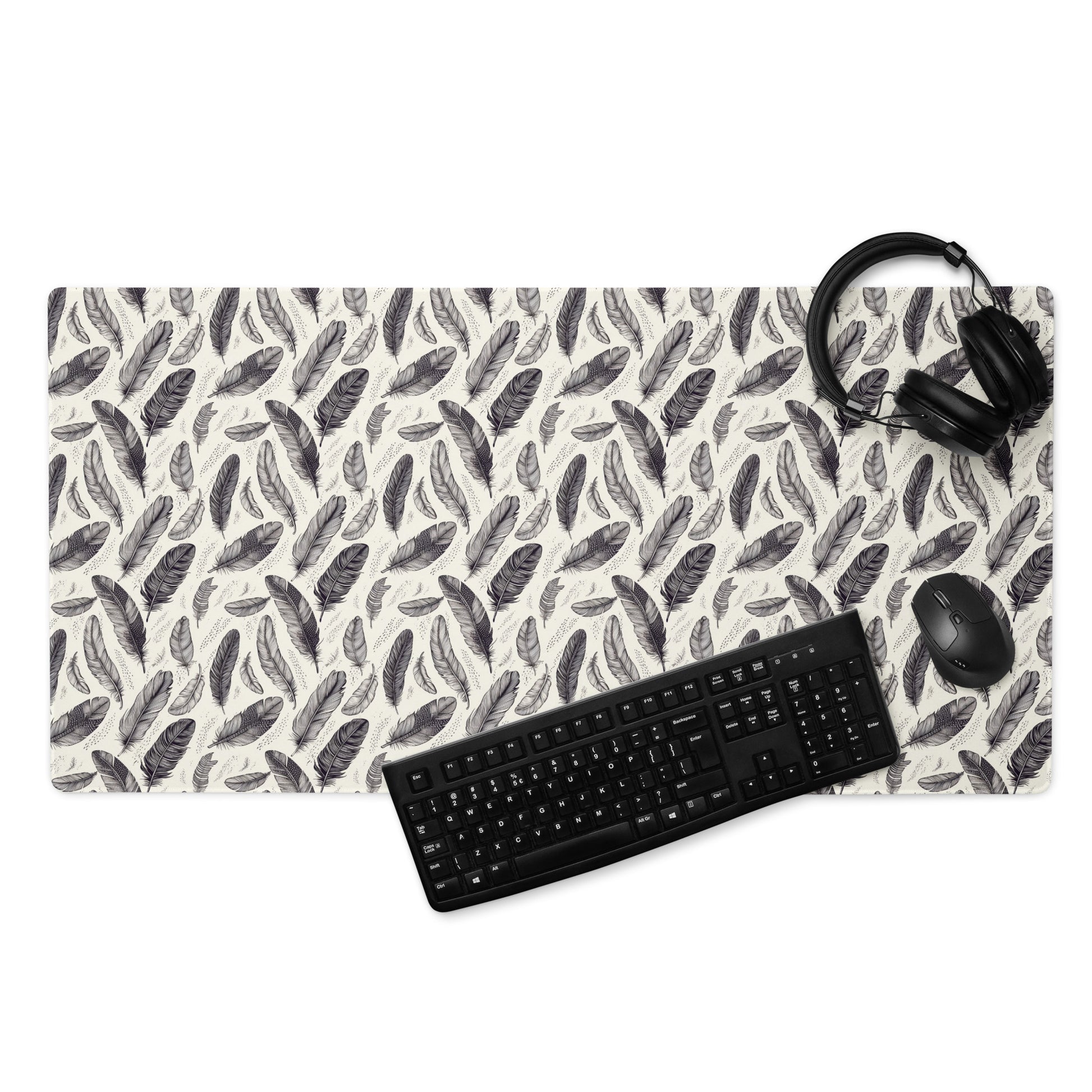 A 36" x 18" gaming desk pad with black and white feathers. A keyboard, mouse, and headphones sit on it.