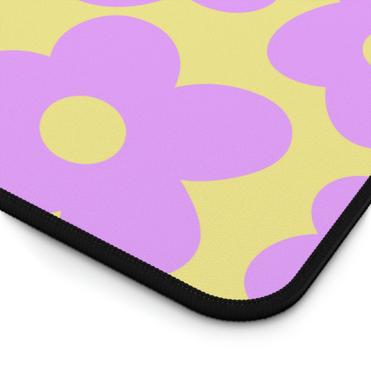 The corner of a 12" x 18" desk mat with purple flowers on a yellow background.