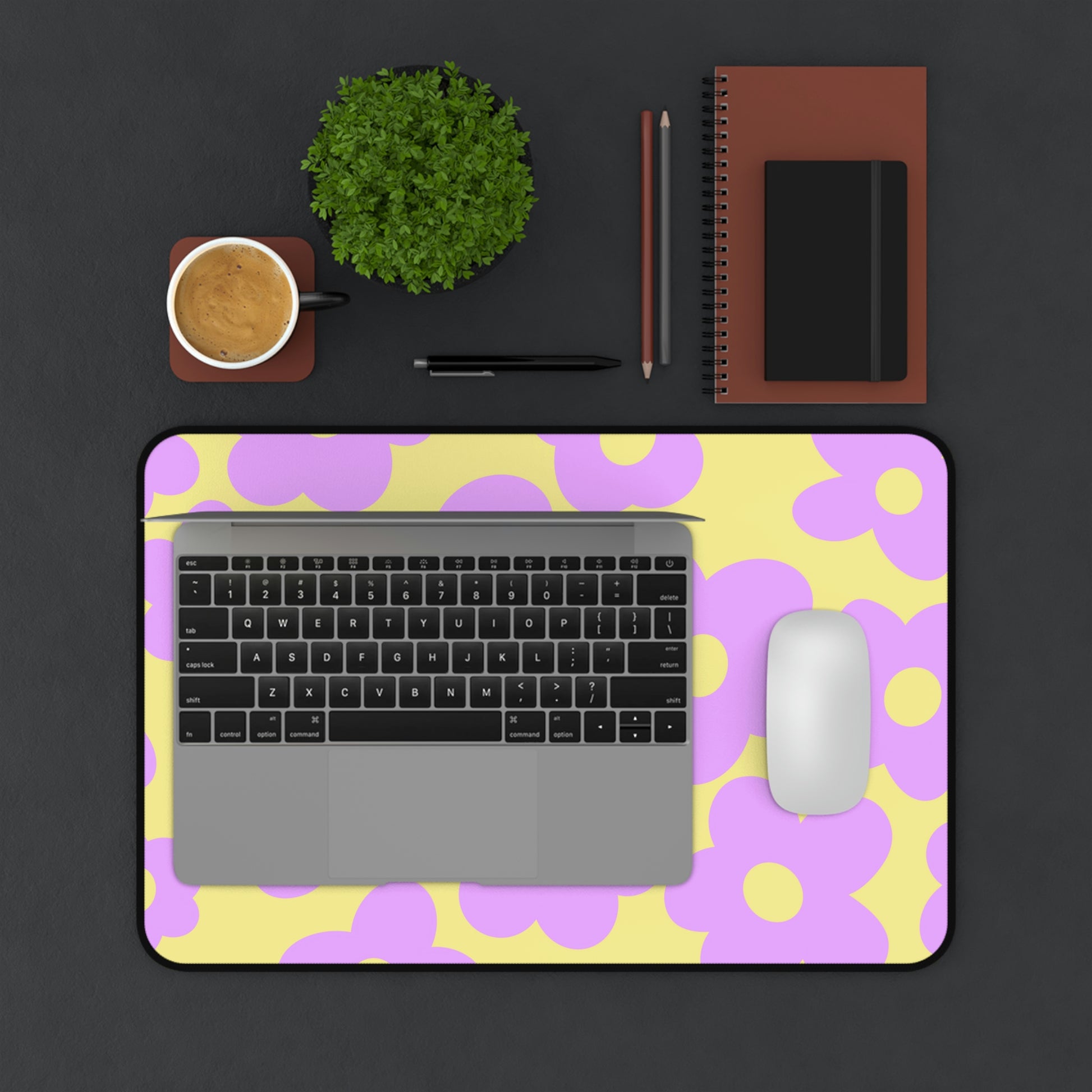 A 12" x 18" desk mat with purple flowers on a yellow background. A laptop and mouse sit on top of it.