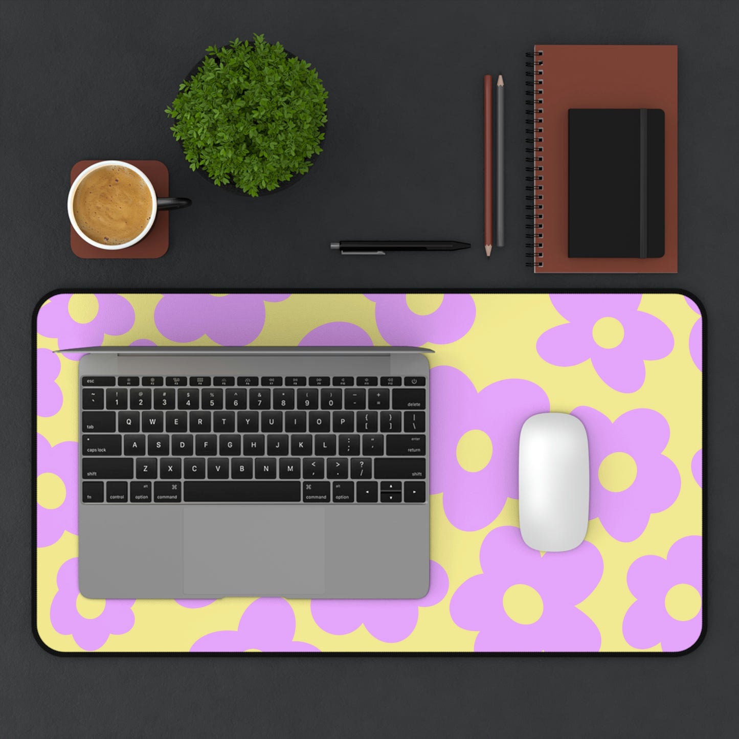 A 12" x 22" desk mat with purple flowers on a yellow background. A laptop and mouse sit on top of it.