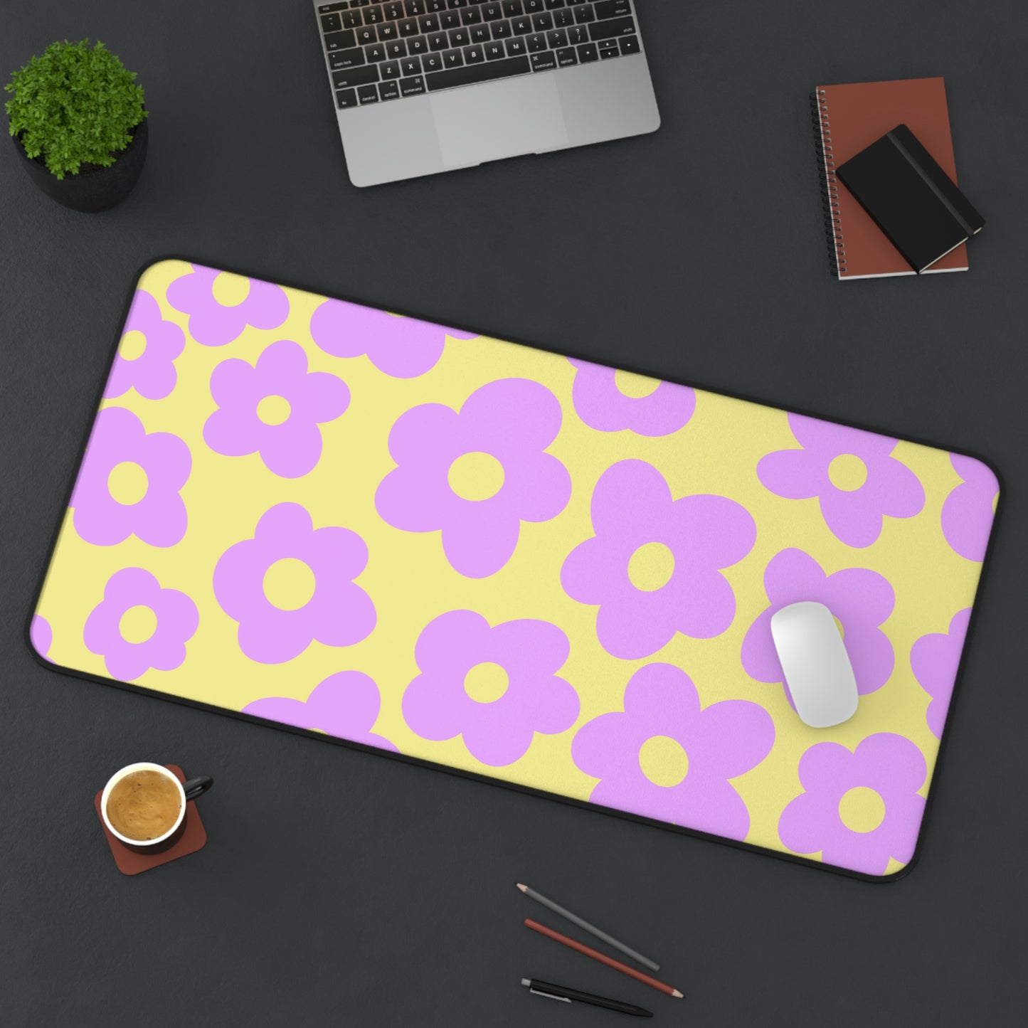 A 31" x 15.5" desk mat with purple flowers on a yellow background sitting at an angle.