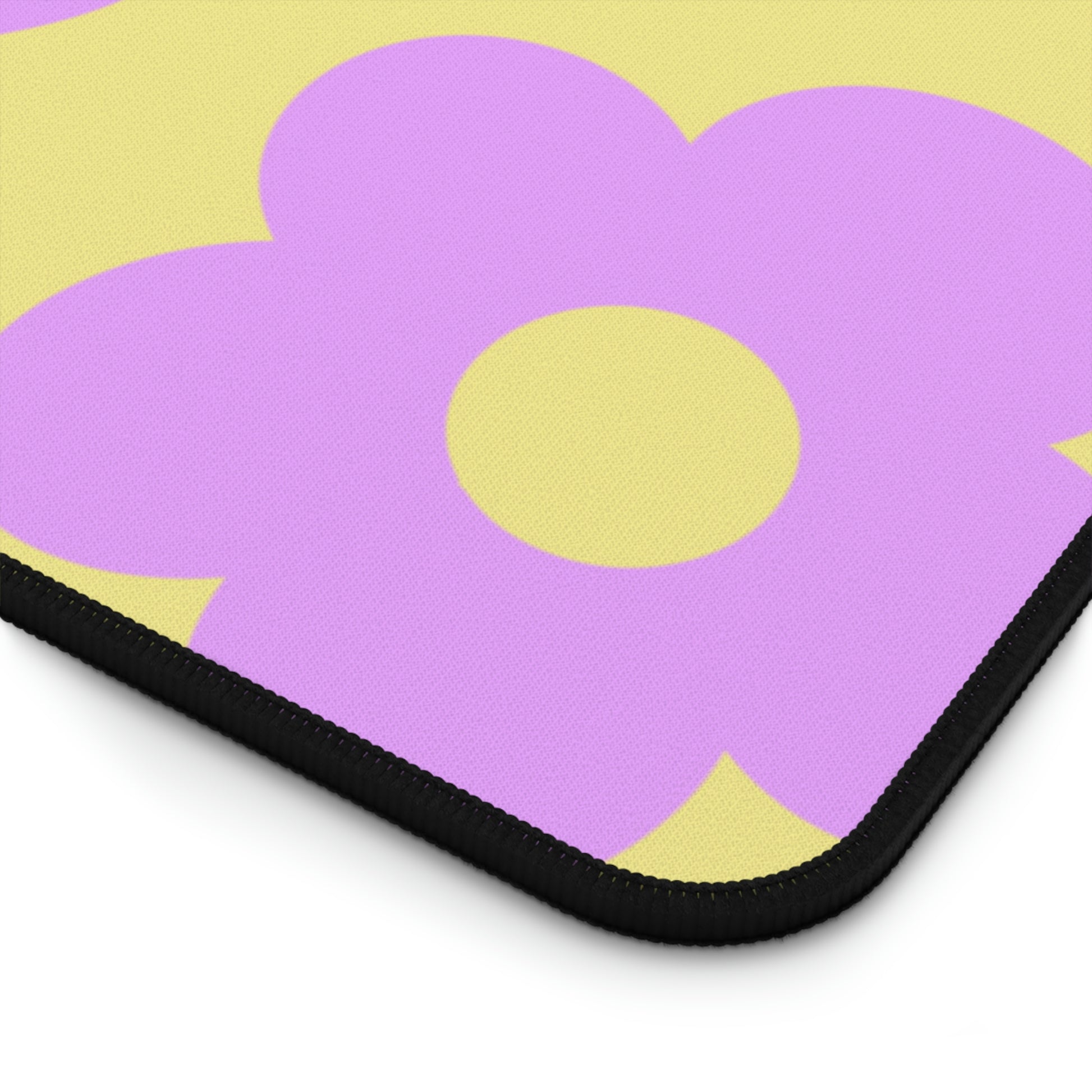 The corner of a 31" x 15.5" desk mat with purple flowers on a yellow background.