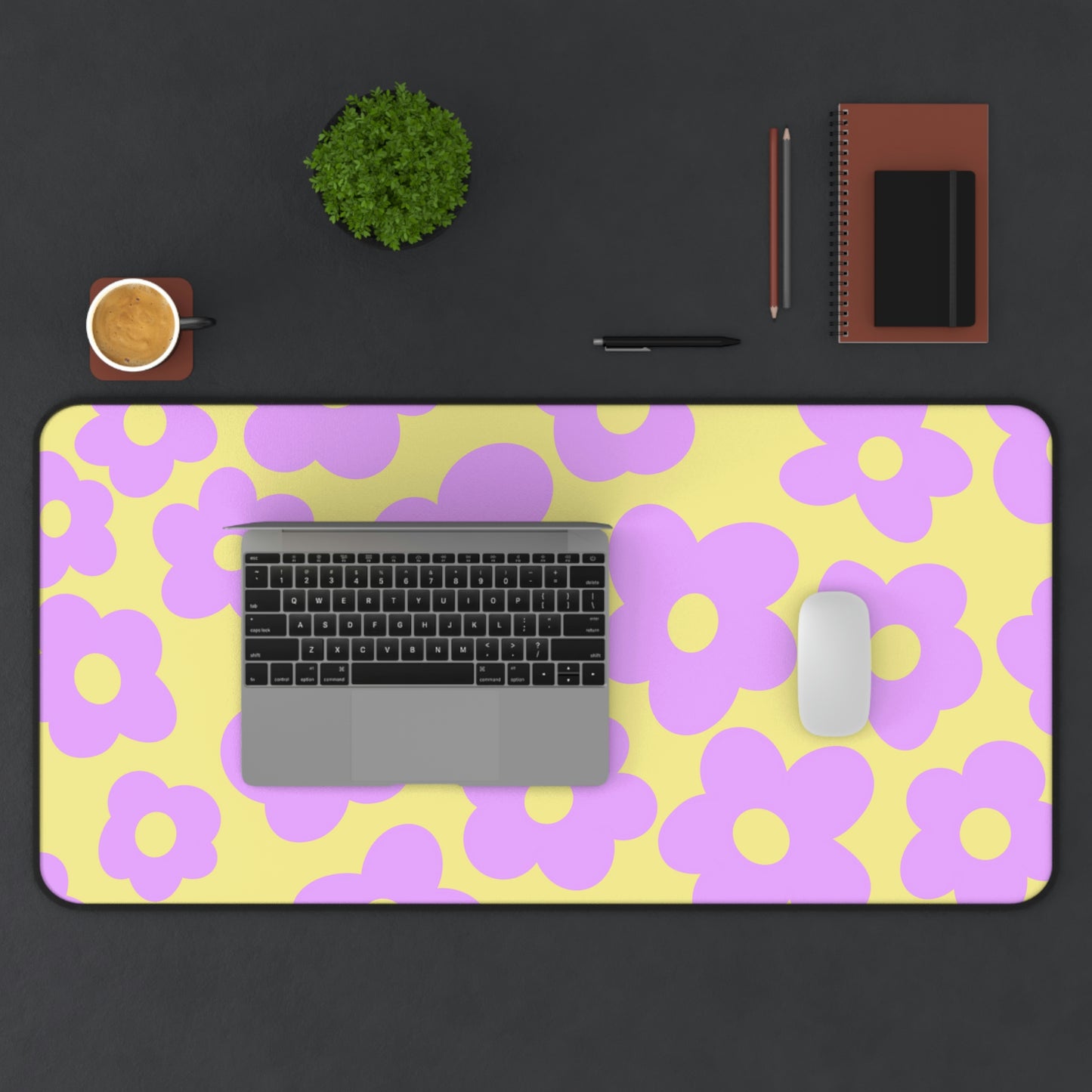 A 31" x 15.5" desk mat with purple flowers on a yellow background. A laptop and mouse sit on top of it.