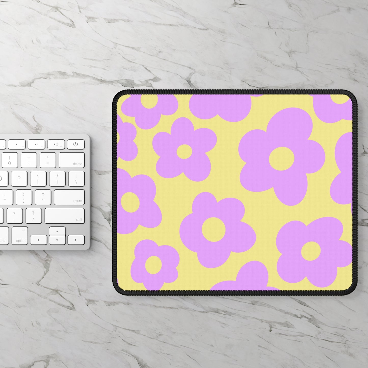 A gaming mouse pad with purple flowers on a yellow background sitting next to a keyboard.