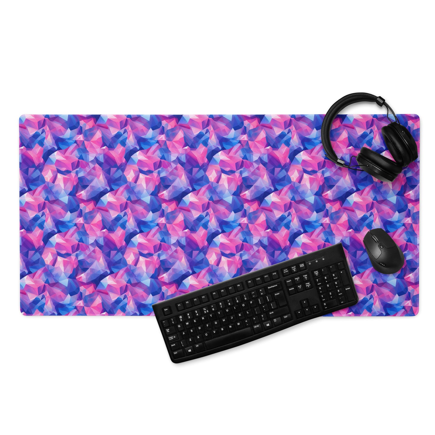 A 36" x 18" gaming desk pad with pink and blue crystals. A keyboard, mouse, and headphones sit on it.