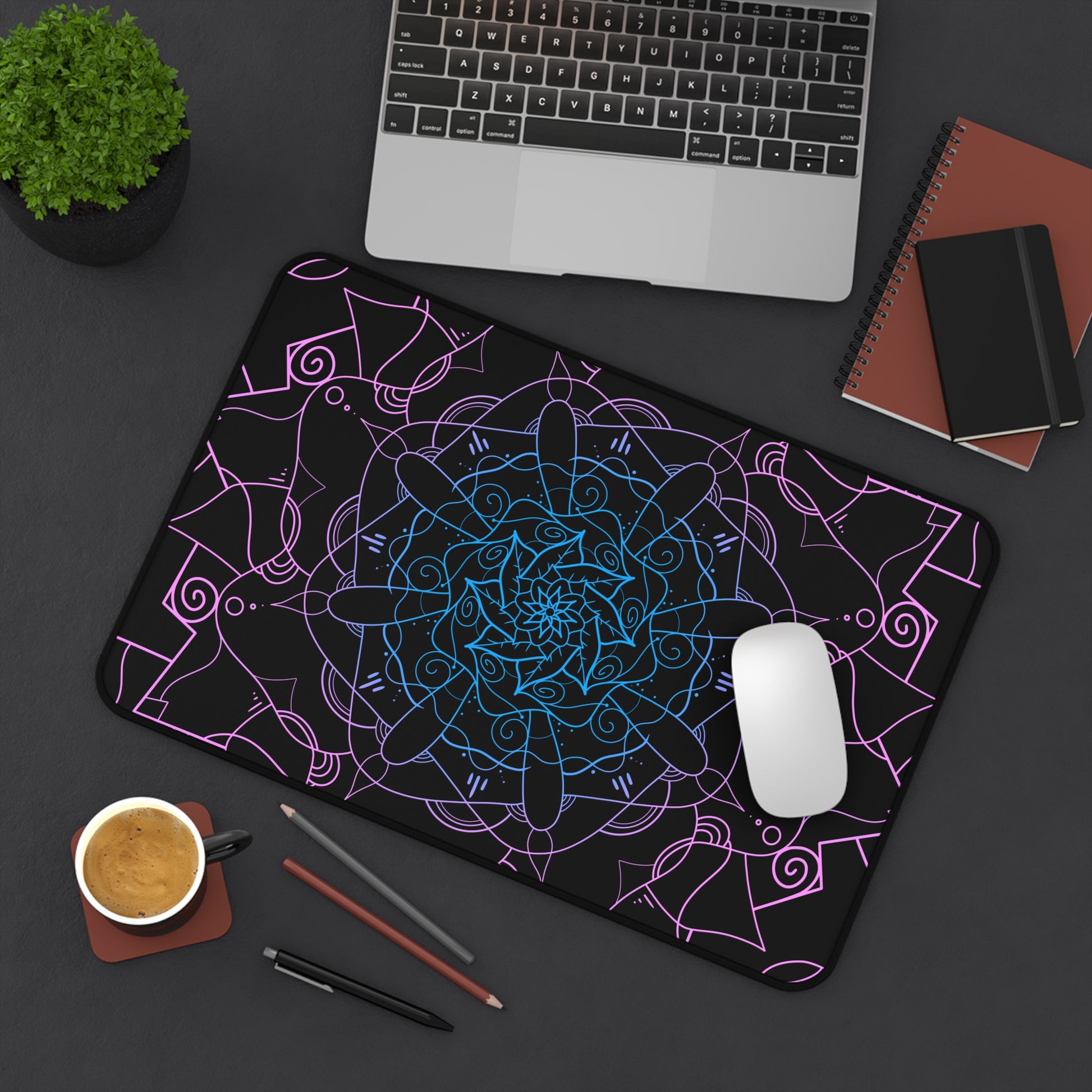 A 12" x 18" desk mat with a pink and blue mandala pattern on a black background sitting at an angle.