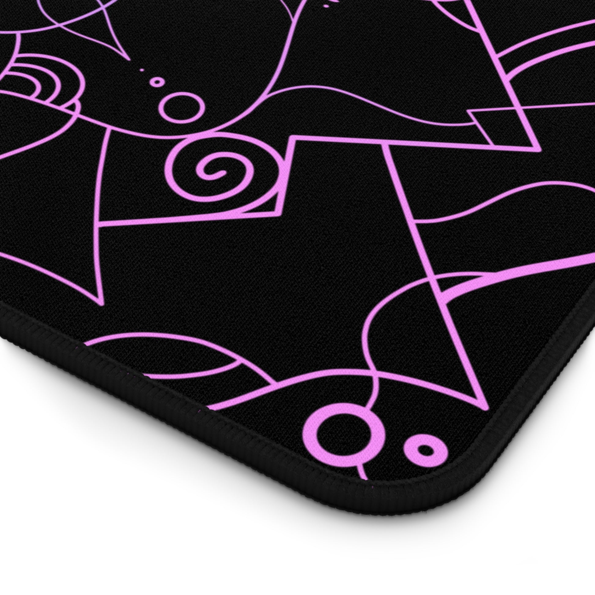 The corner of a 12" x 22" desk mat with a pink and blue mandala pattern on a black background.