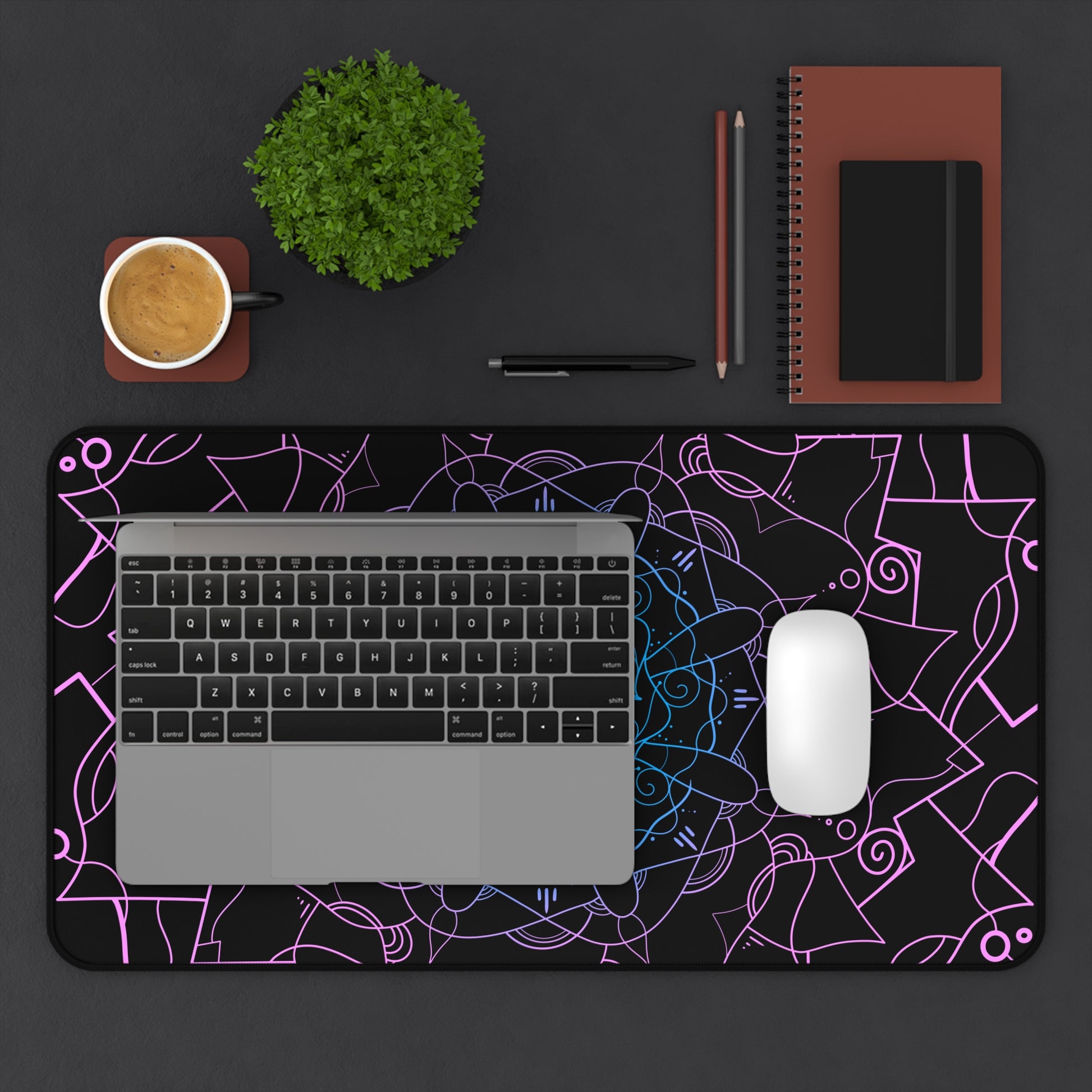 A 12" x 22" desk mat with a pink and blue mandala pattern on a black background. A laptop and mouse sit on top of it.