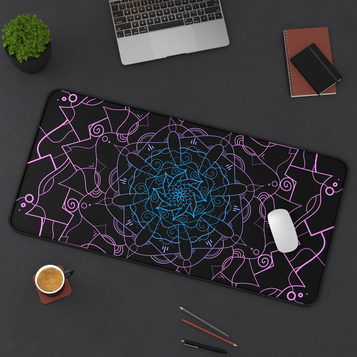A 31" x 15.5" desk mat with a pink and blue mandala pattern on a black background sitting at an angle.