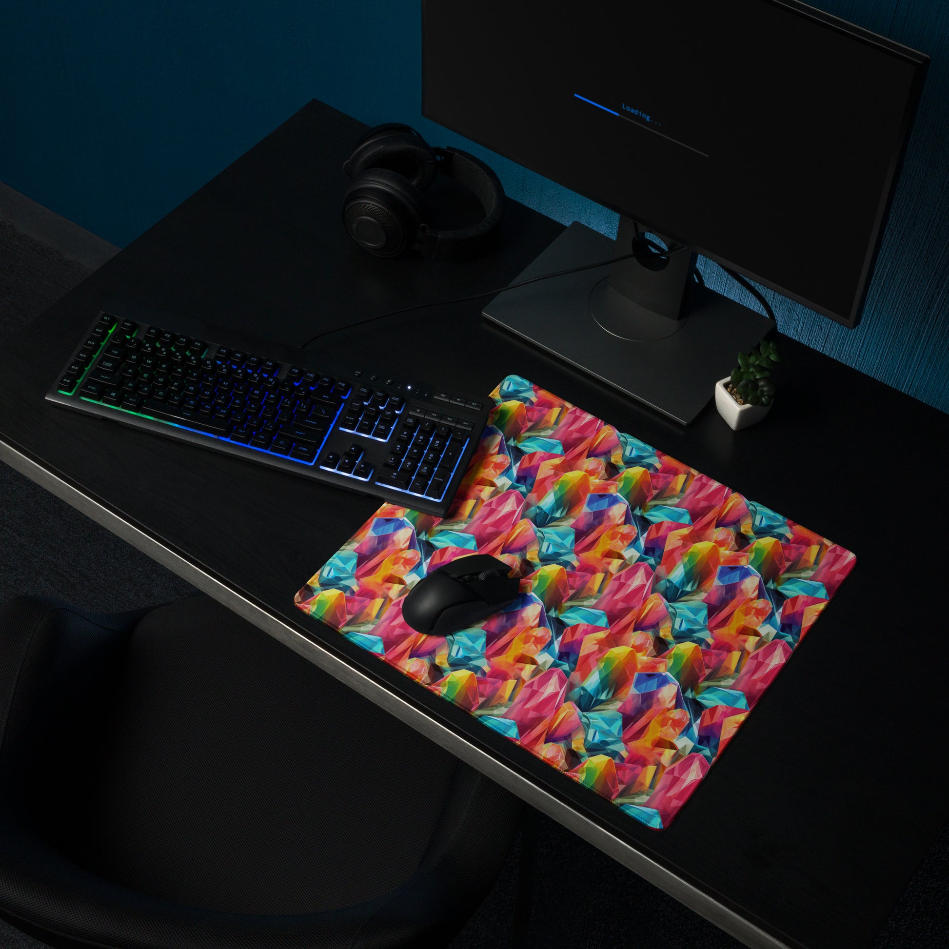 An 18" x 16" gaming desk pad with rainbow crystals. It sits on a black desk with a monitor, keyboard, and mouse.