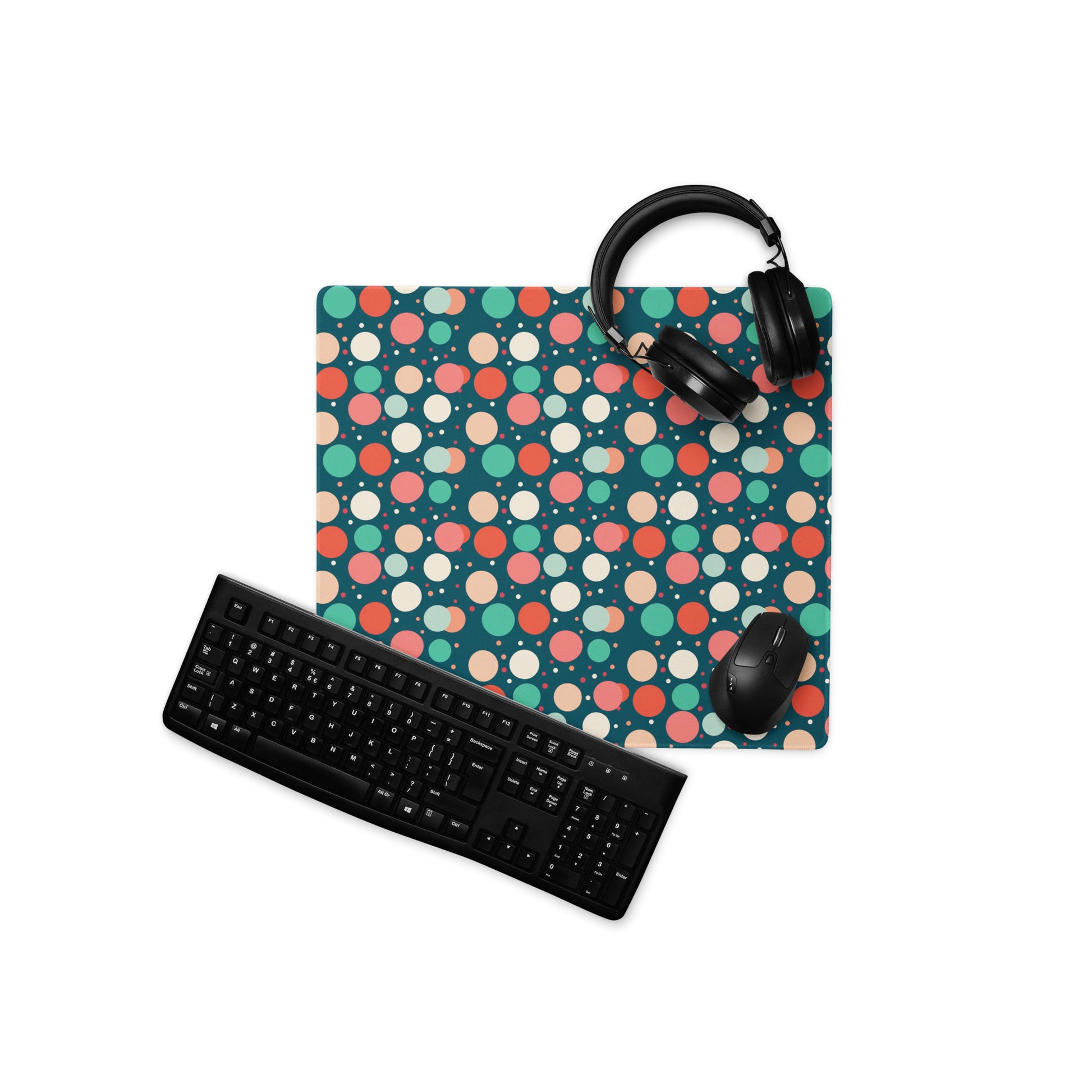  A 18" x 16" desk pad with red teal and yellow polka dot pattern. With a keyboard, mouse, and headphones sitting on it.