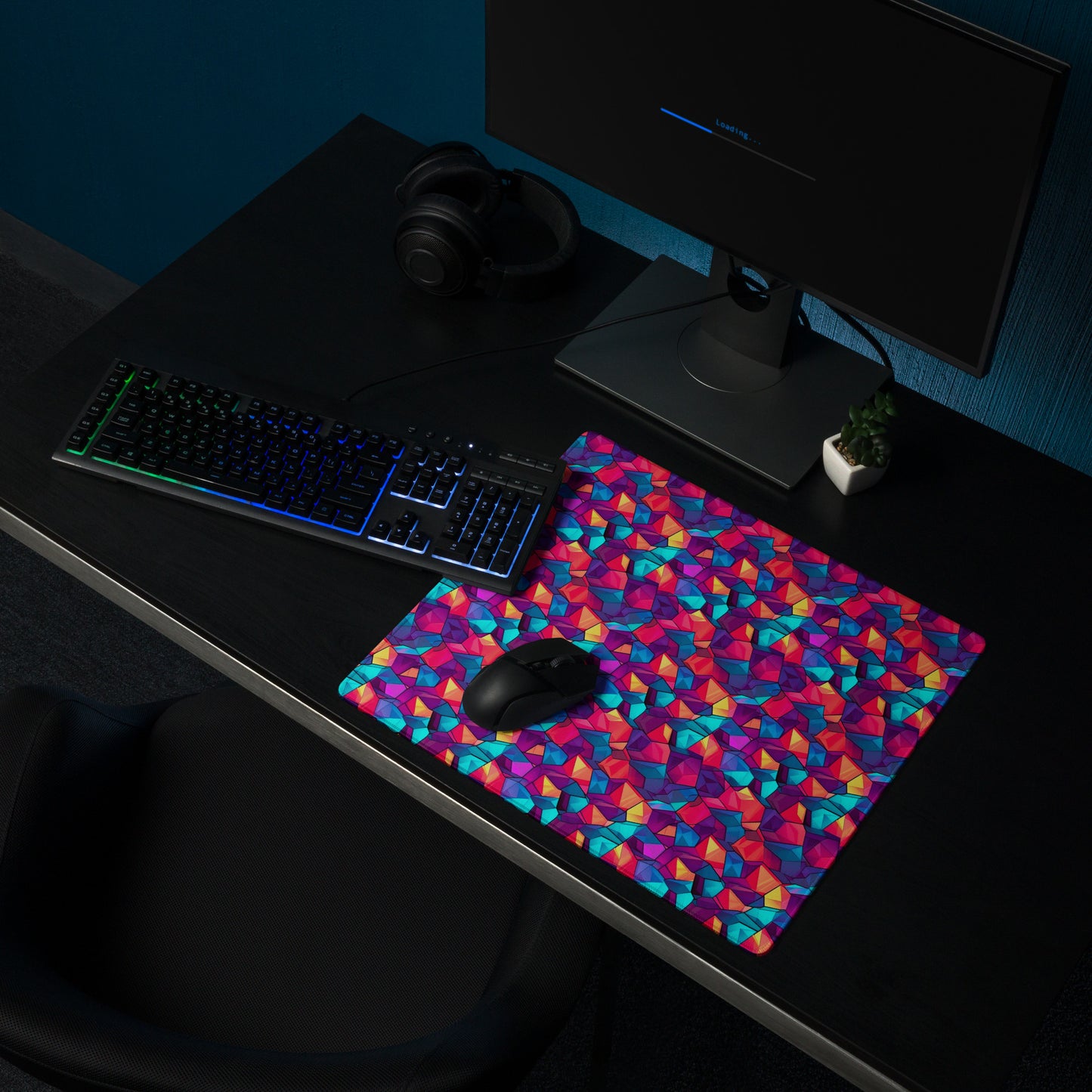 An 18" x 16" gaming desk pad with red, blue, and purple crystals. It sits on a black desk with a keyboard, monitor, and mouse.