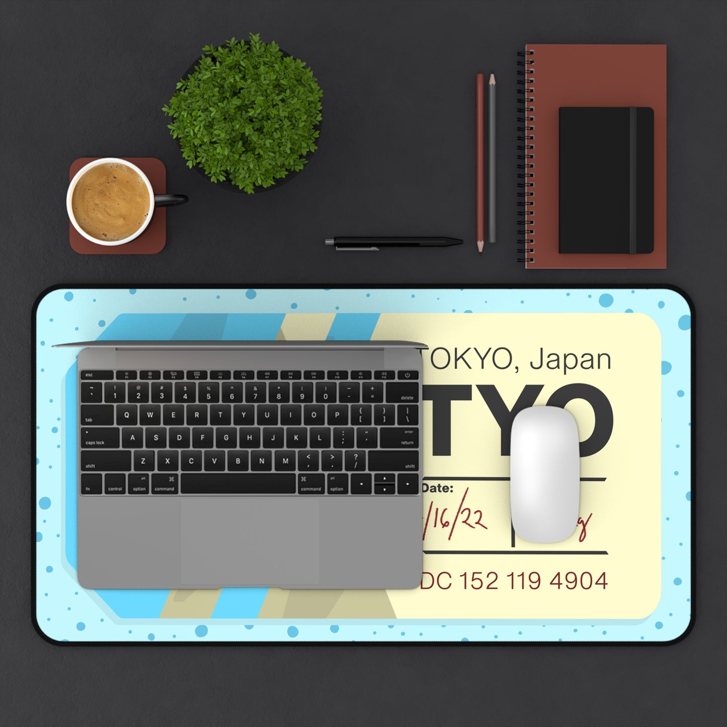A 12" x 22" desk mat with a dotted blue background and a blue and yellow Tokyo airline baggage tag on it. A laptop and mouse sit on top of it.